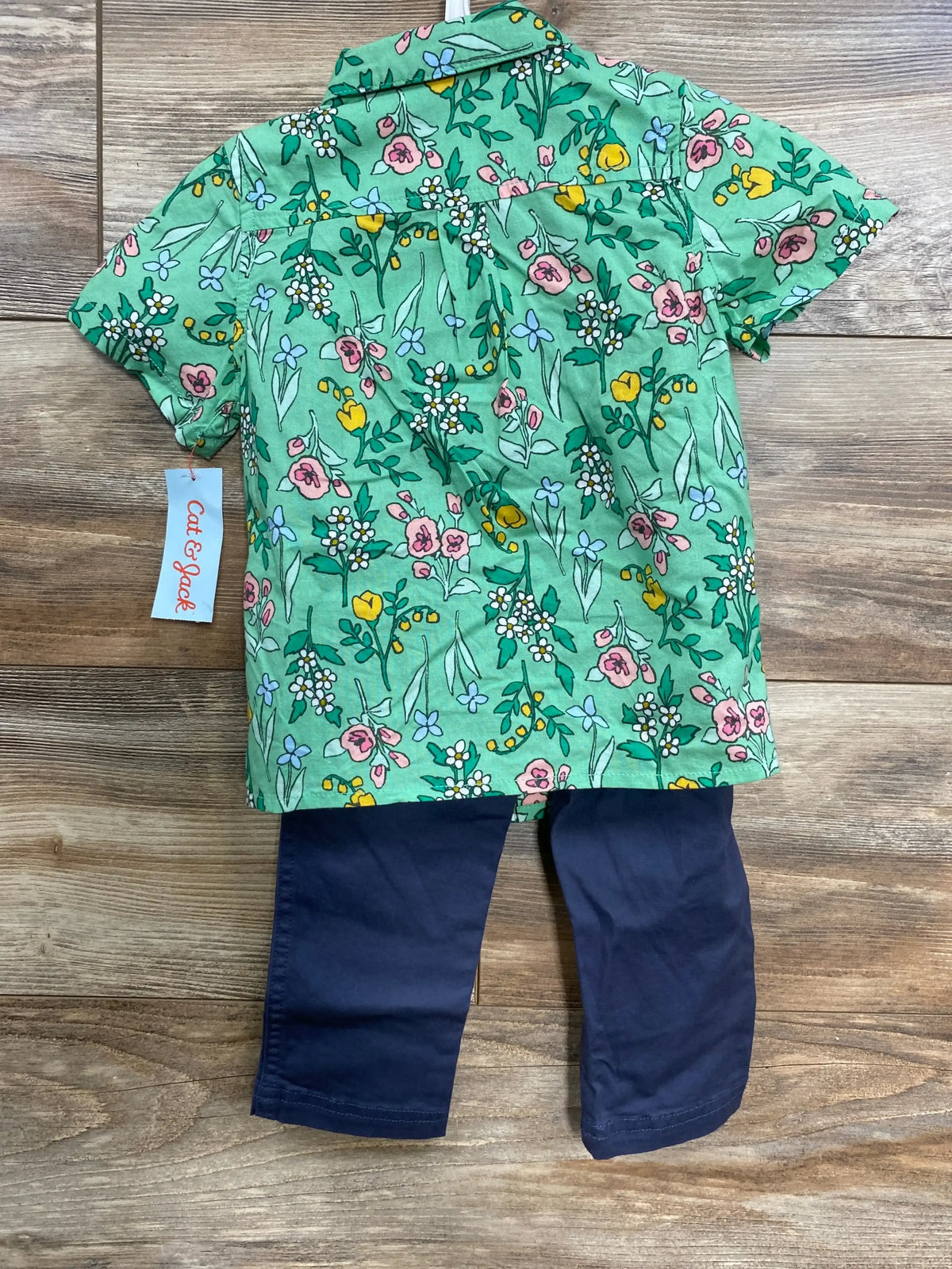 Flat lay of Cat & Jack toddler 3-piece set: green floral short-sleeve button-up with gray bow tie and navy pants on wood