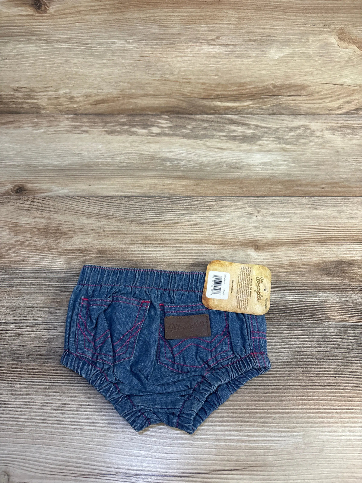 Front view of Wrangler denim bloomers showcasing blue denim, pink stitching, pockets, and elastic waistband on a wood surface