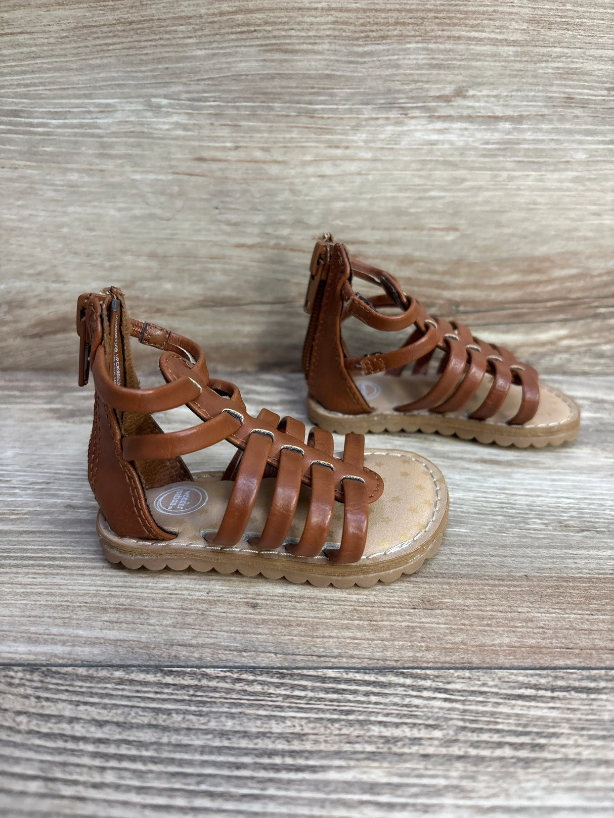 Front-side of Wonder Nation brown toddler gladiator sandal showing multiple straps and back zipper on wood background