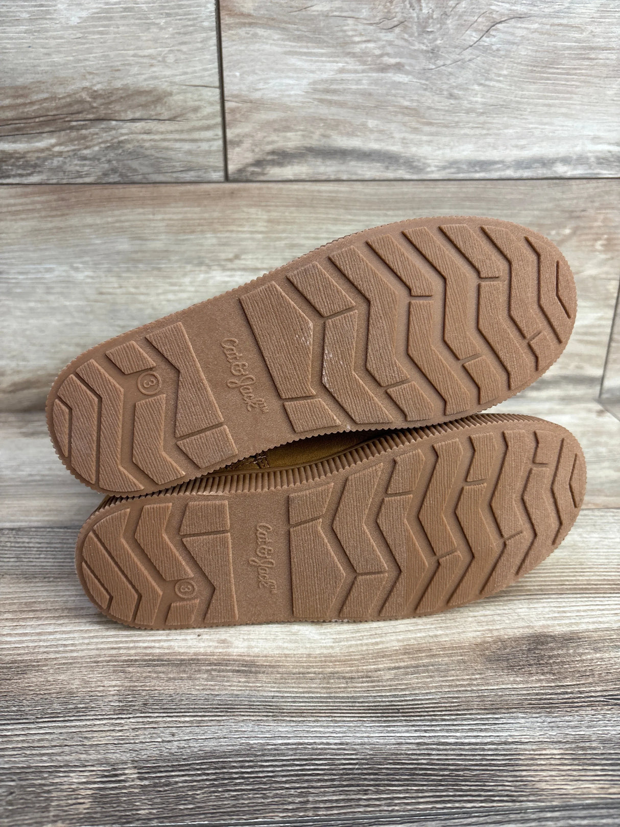 Brown rubber soles of children's shoes with tread pattern, displayed on wood floor
