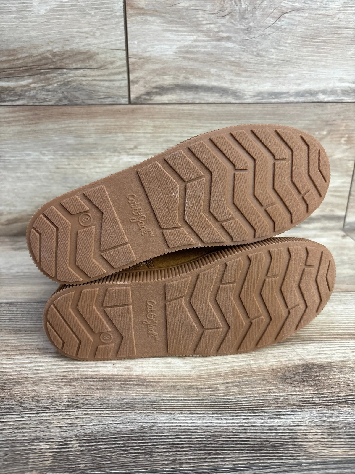 Bottom view of Cat & Jack Natalia kids’ shearling boots (size 3Y) showing brown rubber soles with zigzag tread on wood floor