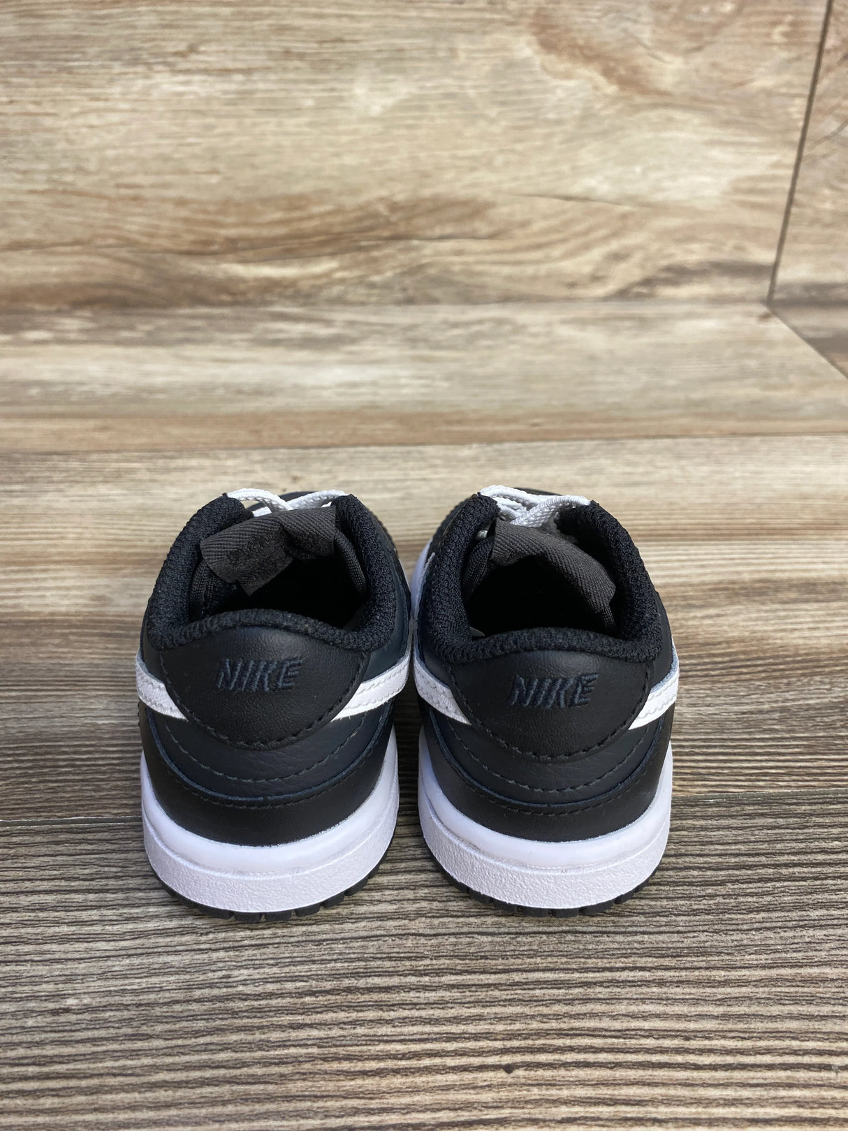Back view of black and white Nike toddler sneakers on wooden floor