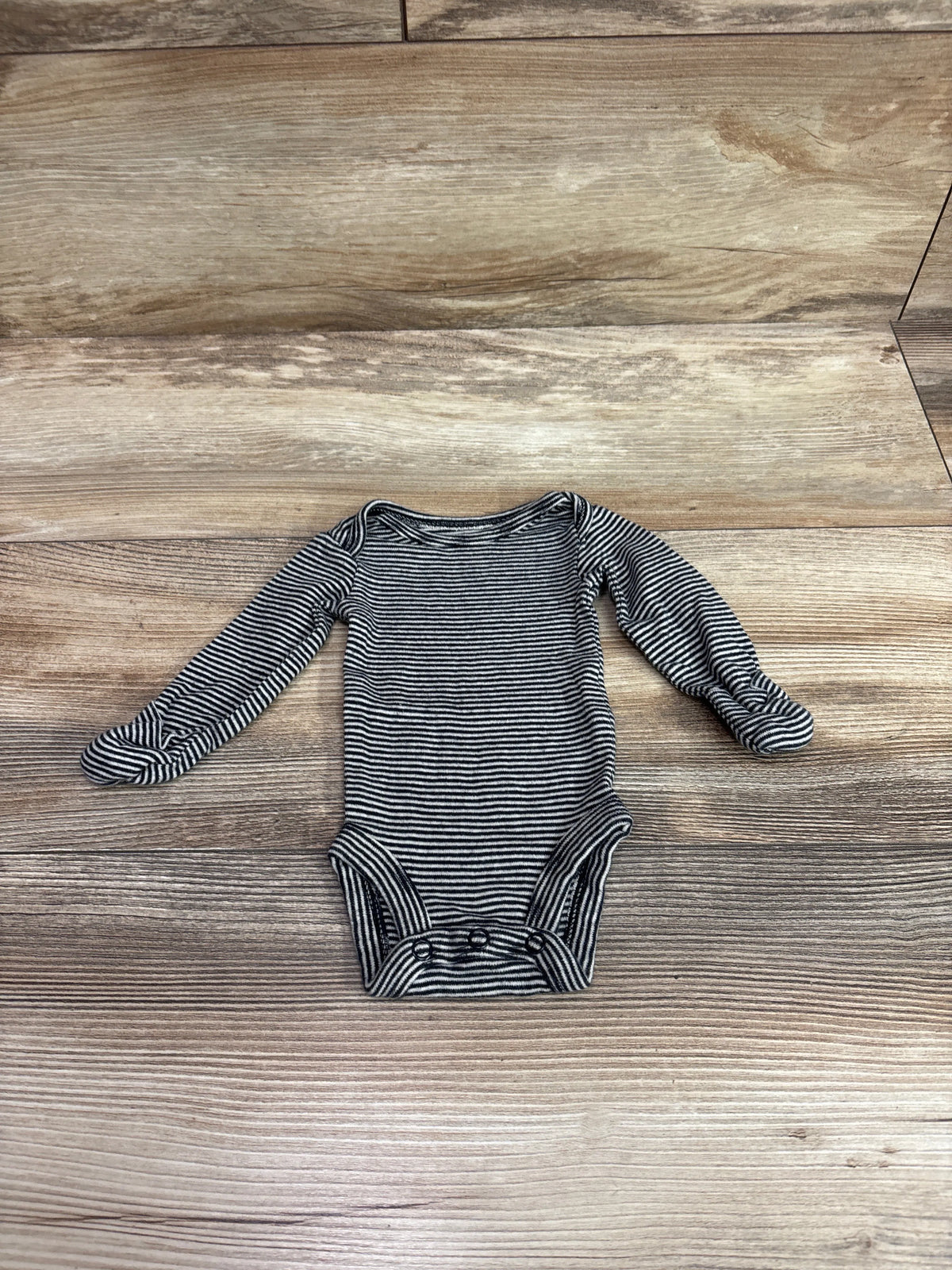 Carter's black and white striped long sleeve baby bodysuit for preemie size on wood floor