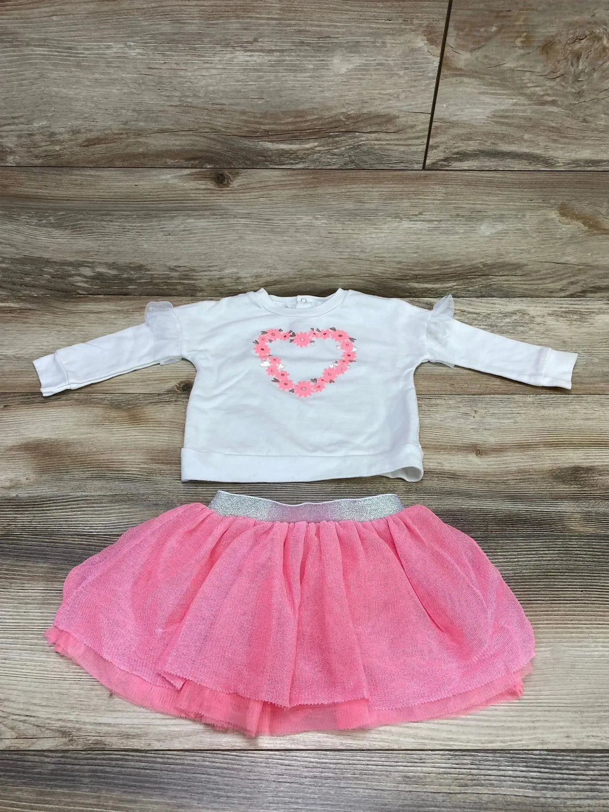 Flat lay of toddler white sweatshirt with pink floral heart and matching pink tulle tutu with silver waistband on wood