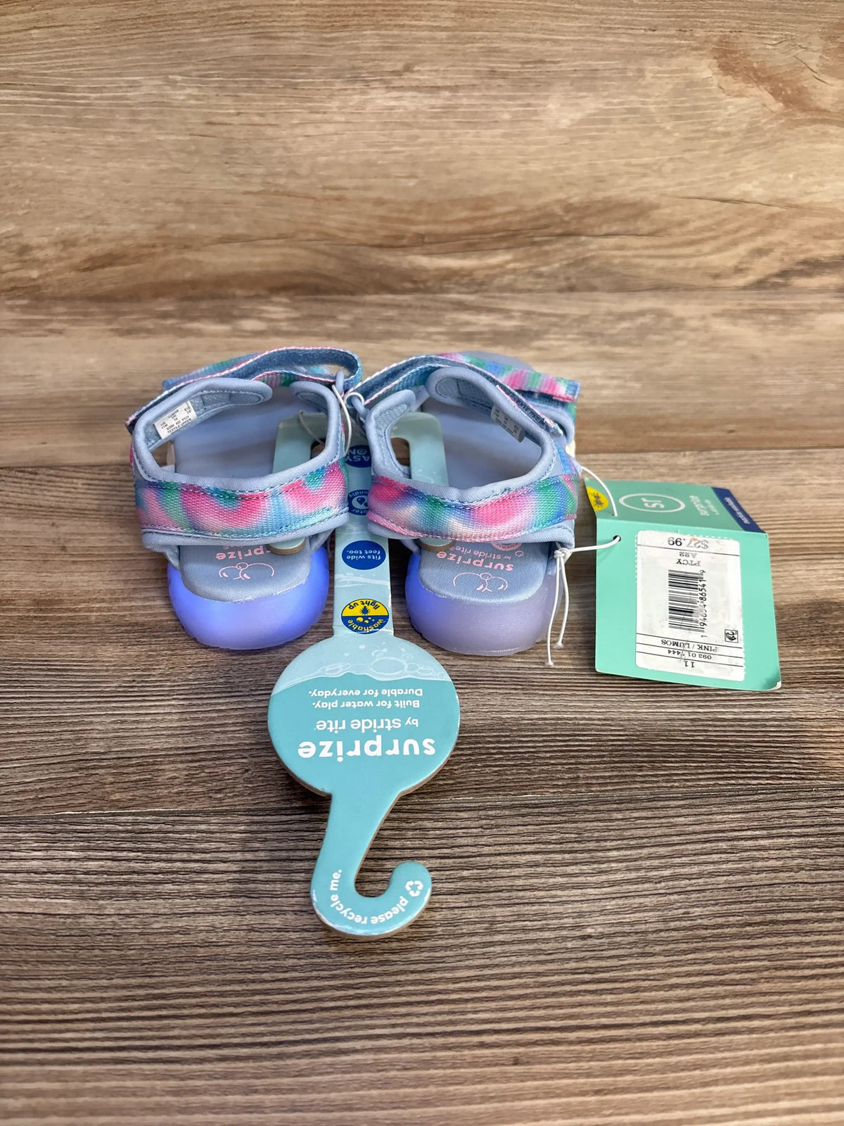 Rear view of toddler Surprize Lumos light-up sandals in blue pastel tie-dye showing illuminated heels and adjustable Velcro straps on wood background