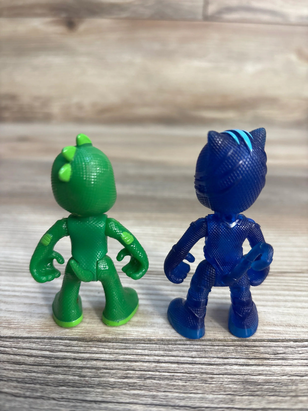 Rear view of PJ Masks Catboy and Gekko action figures 2-pack showing textured plastic details on a wood surface