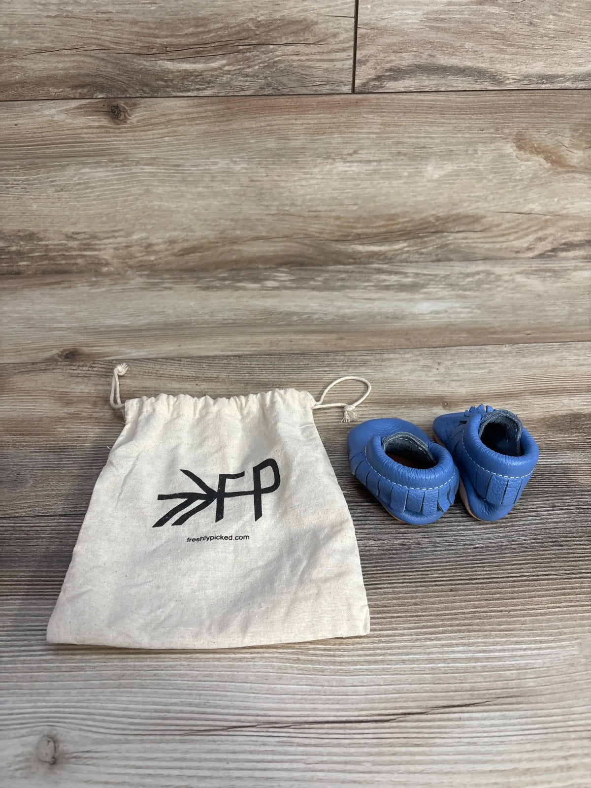 Blue baby moccasins with drawstring Freshly Picked bag on wood floor