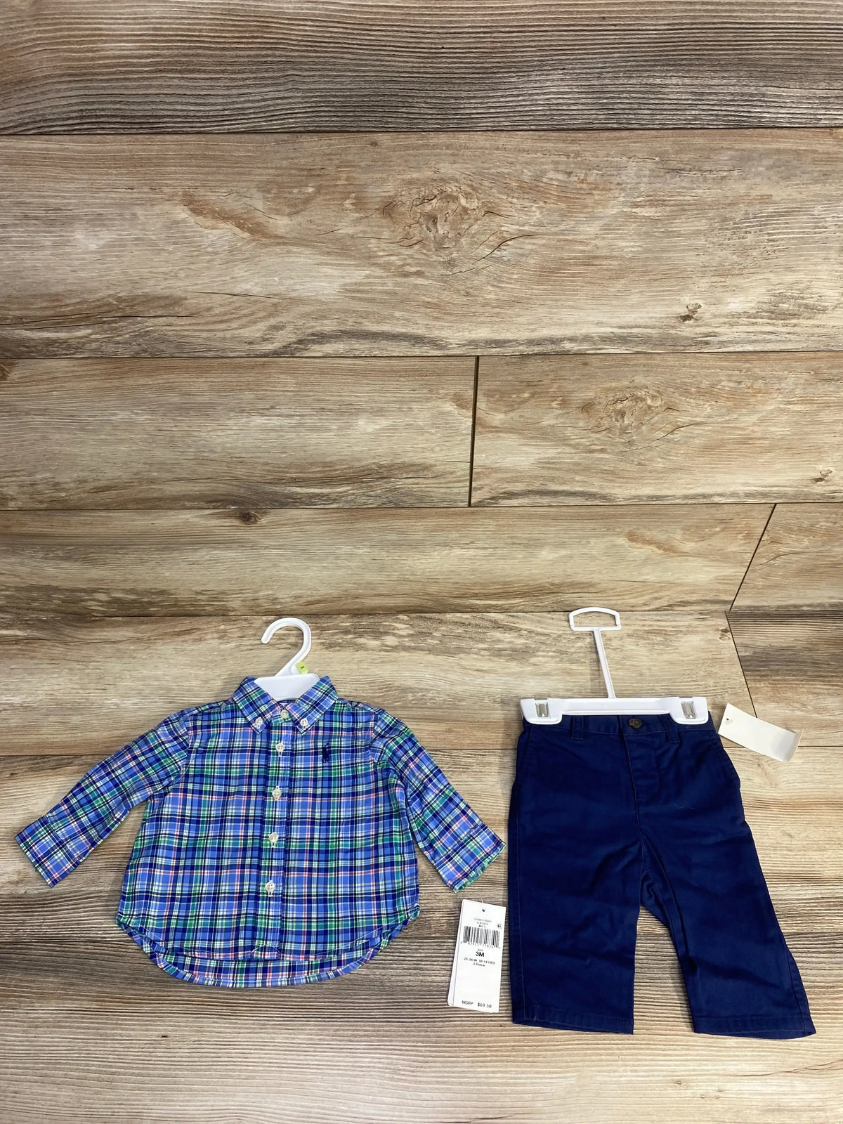 Flat lay of Ralph Lauren 2-piece baby boy size 3M blue-green plaid button-down shirt and navy pants on wood floor