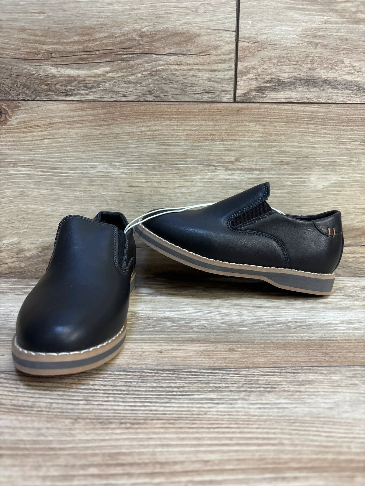 Front three-quarter view of Cat & Jack Neal toddler black slip-on loafers size 11C showing tan contrast soles on wood background