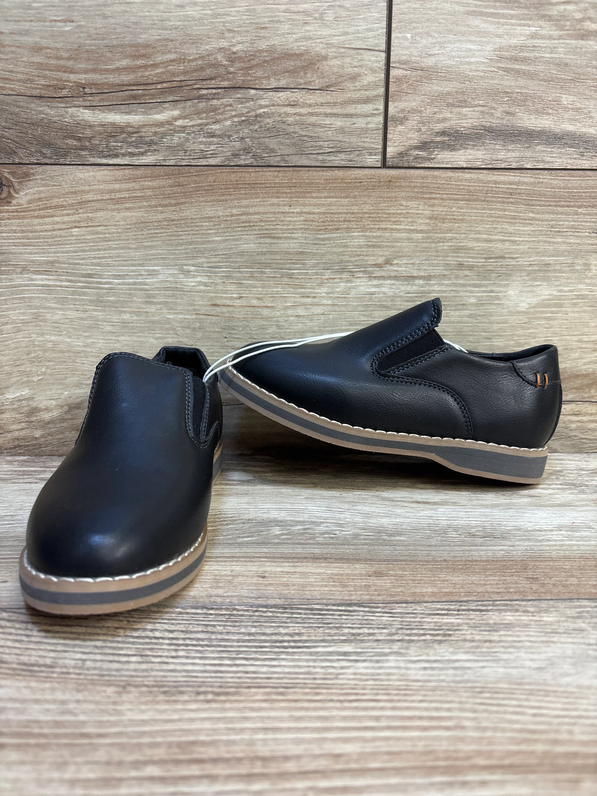 Front three-quarter view of Cat & Jack Neal toddler black slip-on loafers size 11C showing tan contrast soles on wood background