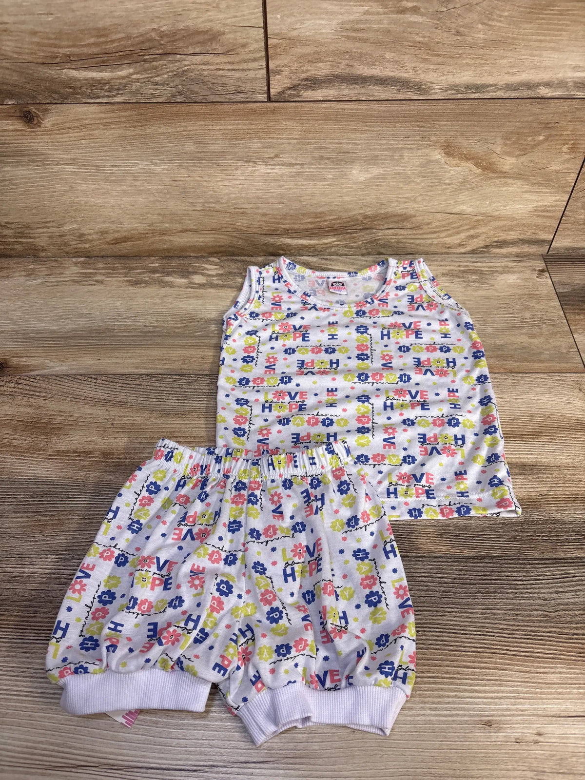 Front view of a white baby tank top and shorts set showcasing coordinating pieces on a wood background
