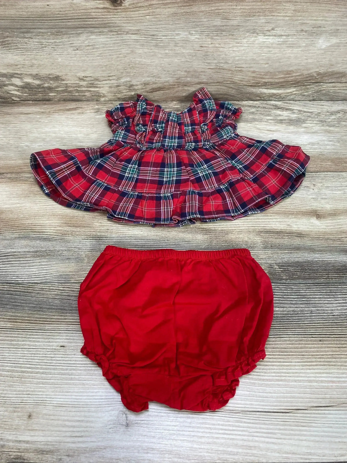Top down view of Janie and Jack two piece red plaid baby set showcasing a ruffled dress and red bloomers on wood grain