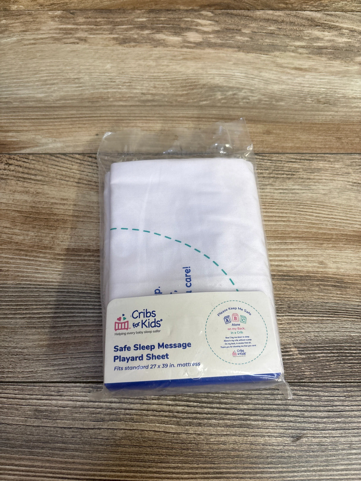 Cribs for Kids Safe Sleep Message Playard Sheet in packaging on wood surface