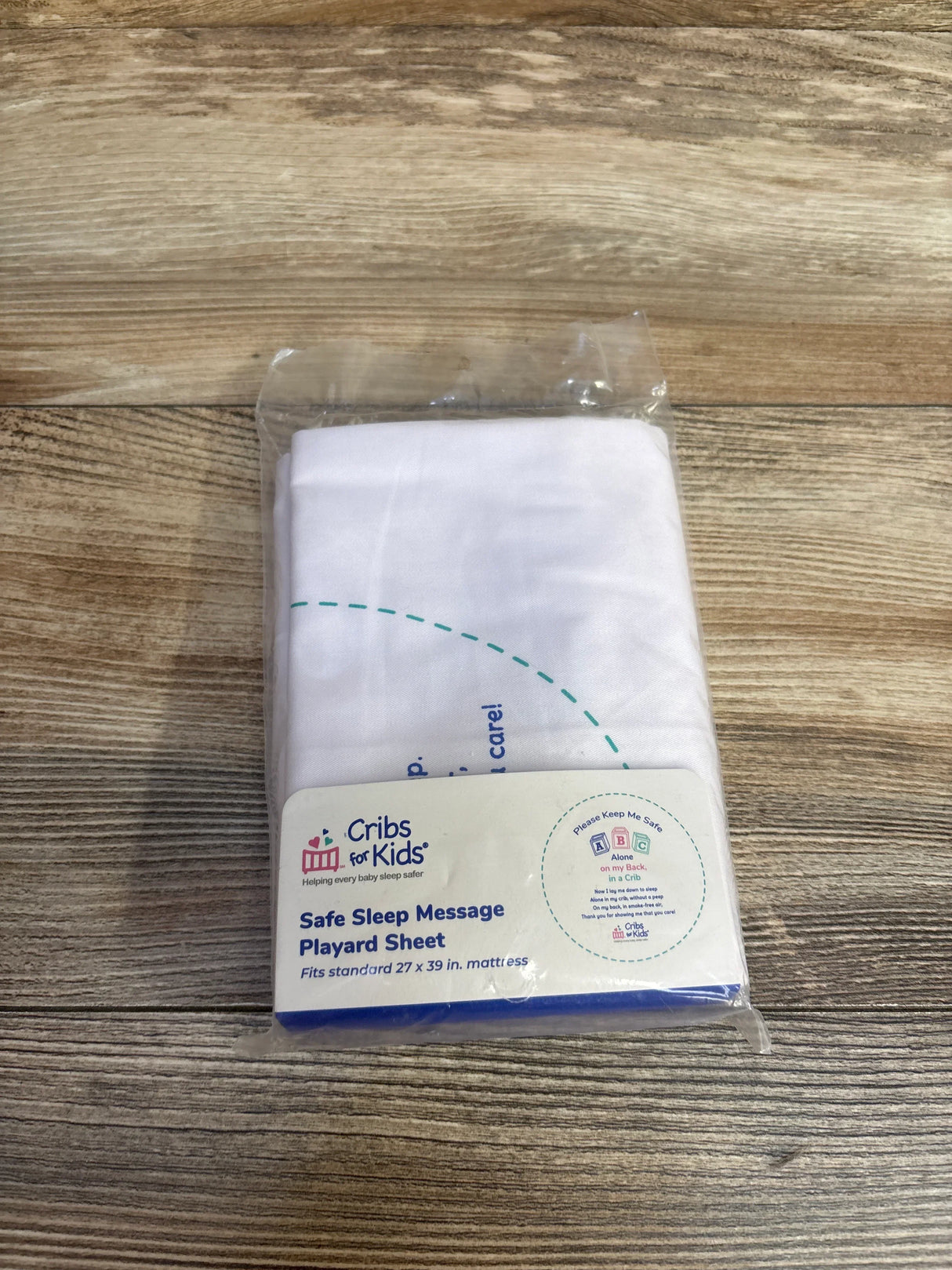 Cribs for Kids Safe Sleep Message Playard Sheet in packaging on wood surface