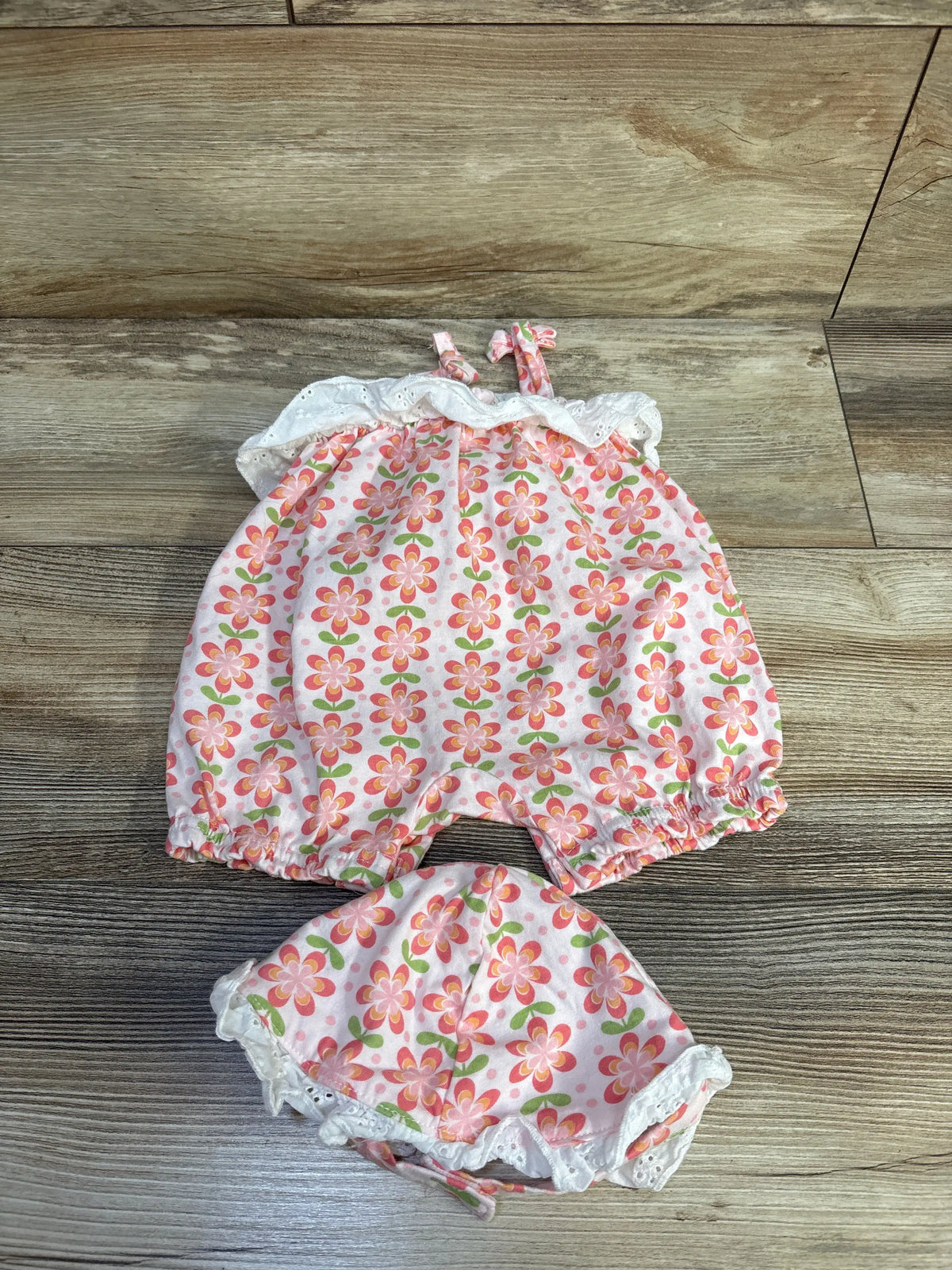 Top view of Charlotte & Star floral tank romper and matching hat showcasing pink flower pattern and white trim on wood floor