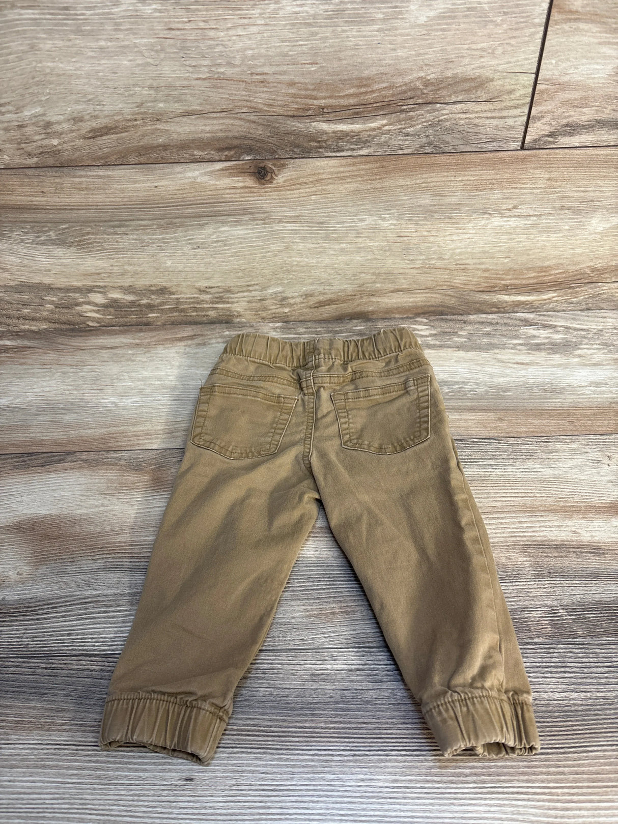 Brown toddler pants with elastic waistband and cuffs on wood background