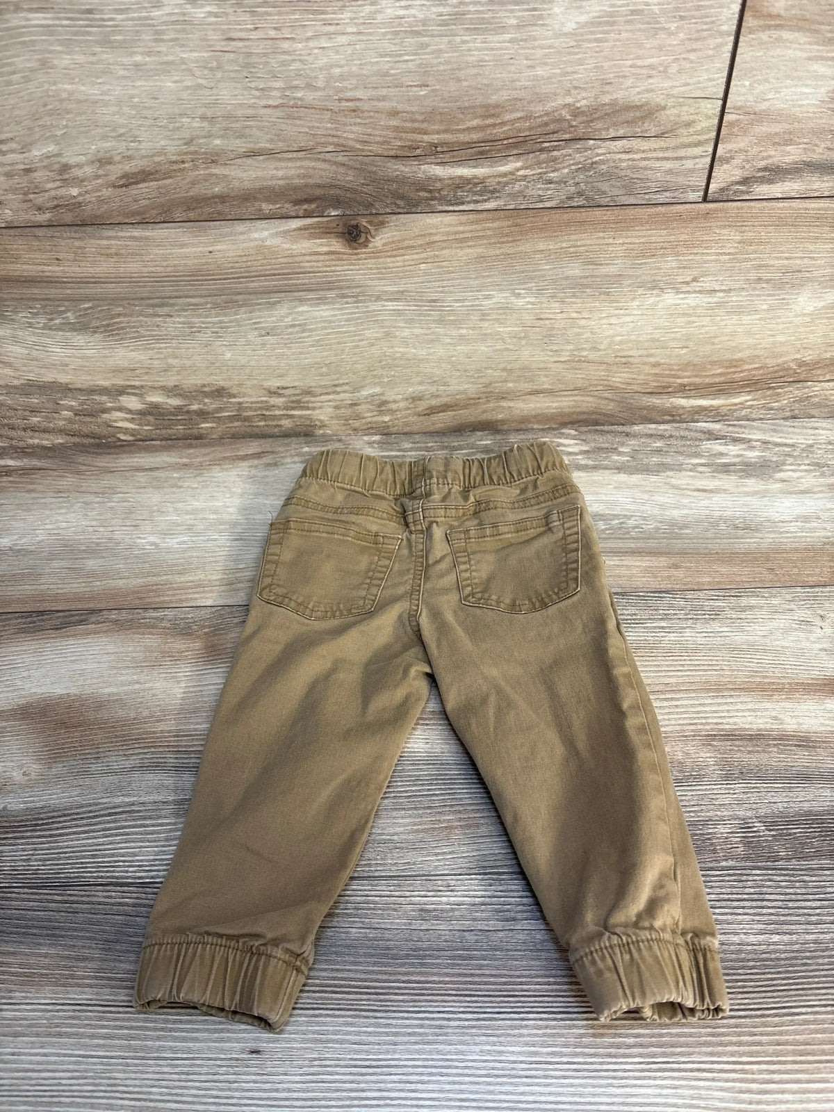 Brown toddler pants with elastic waistband and cuffs on wood background