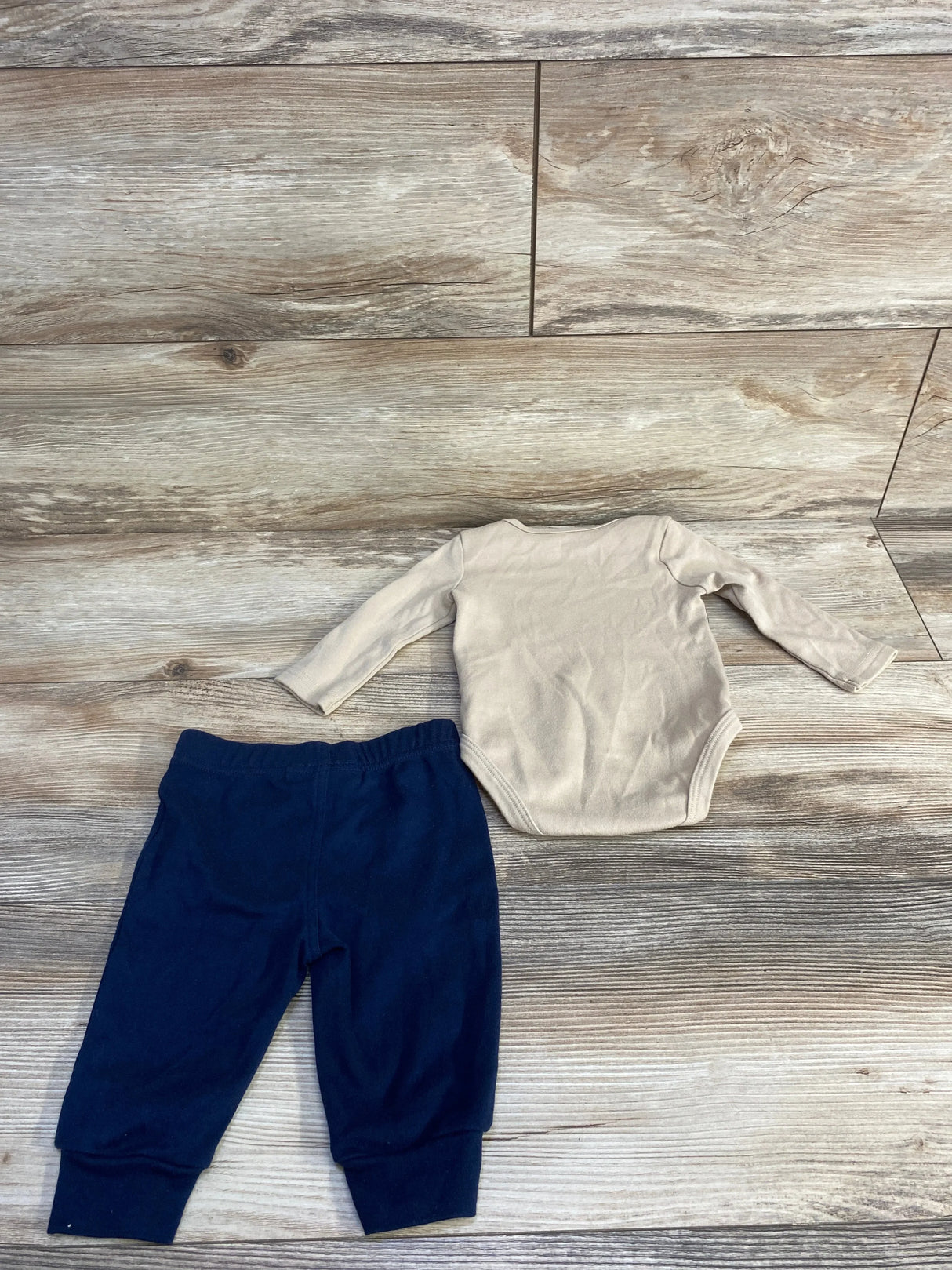 Top-down view of newborn beige Tommy Hilfiger long-sleeve bodysuit (back) with navy elastic-waist pants on light wood background