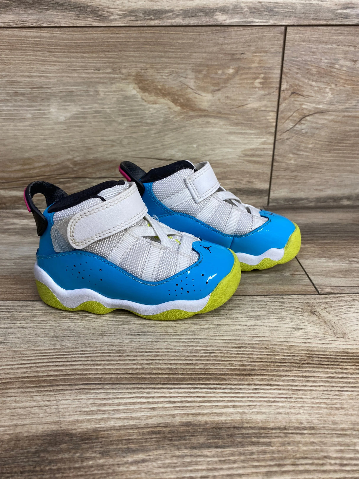 Three-quarter view of Air Jordan 6 Rings TD sneakers showcasing white and light blue fury uppers with hook and loop strap and yellow soles on wood plank floor