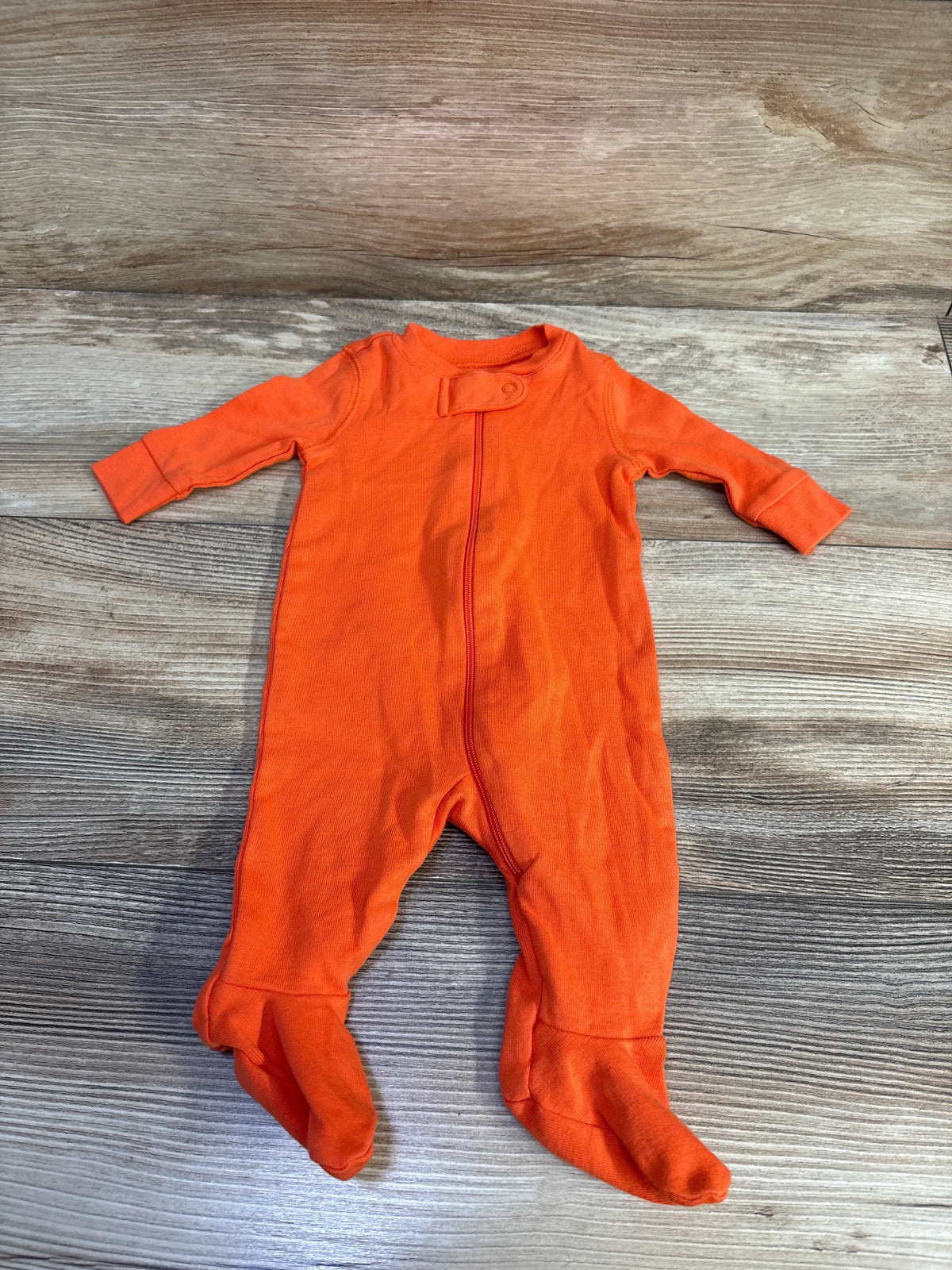 Front view of orange Primary Organic Solid Sleeper with full-length zipper, long sleeves, and footies on wood-grain background