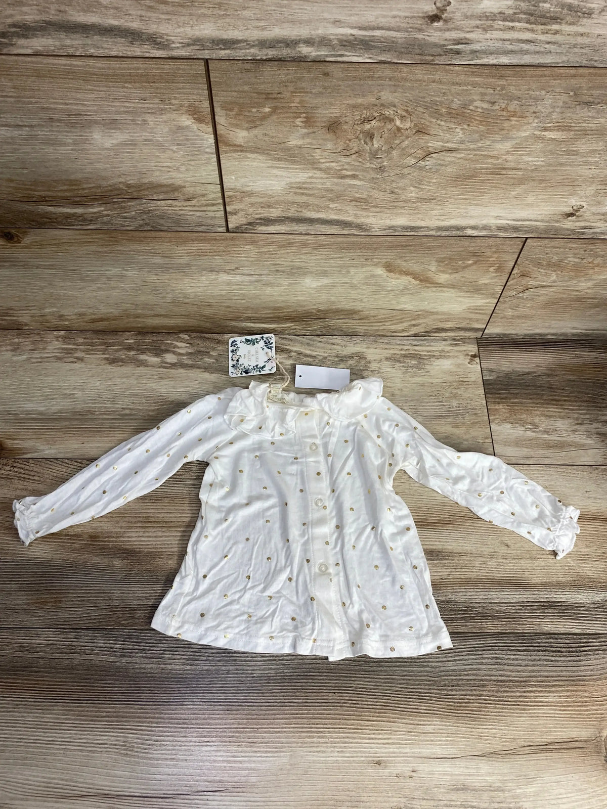 White long sleeve baby shirt with gold polka dots and ruffled collar on wood background