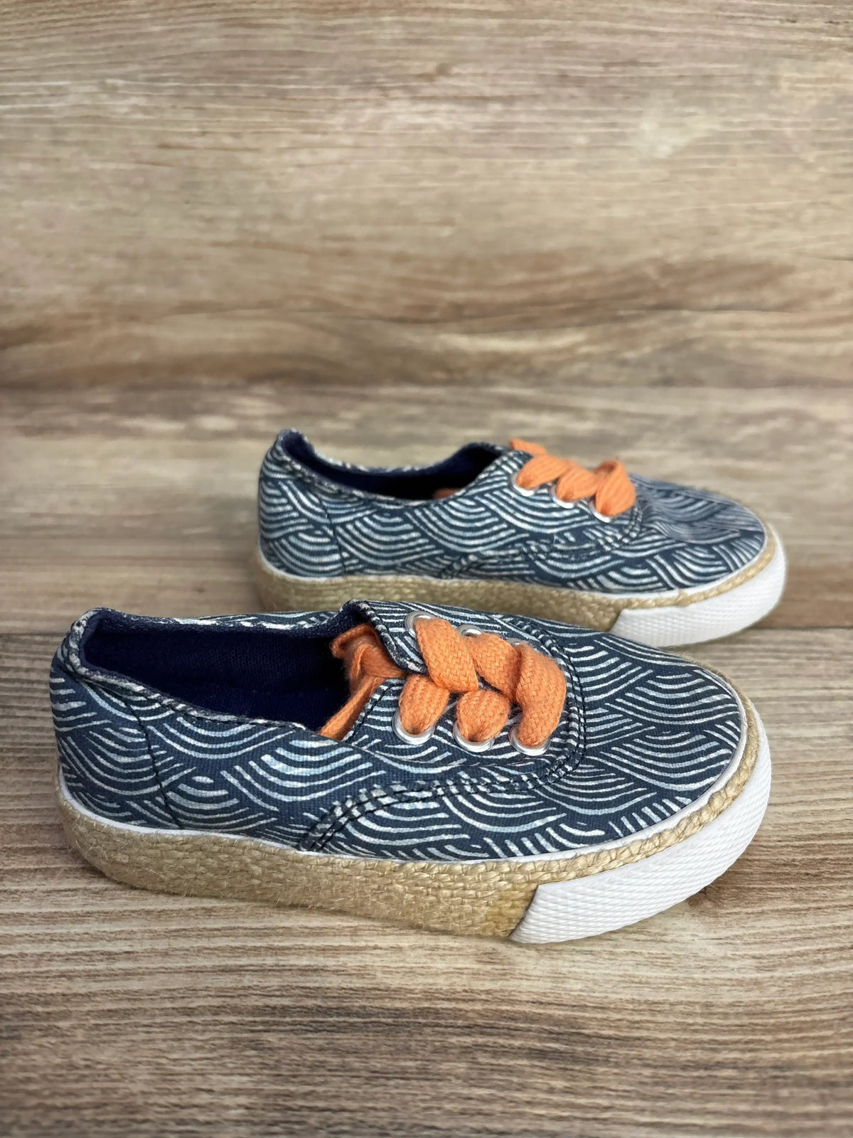 Pair of navy blue toddler shoes with white wave patterns and orange laces on wooden floor