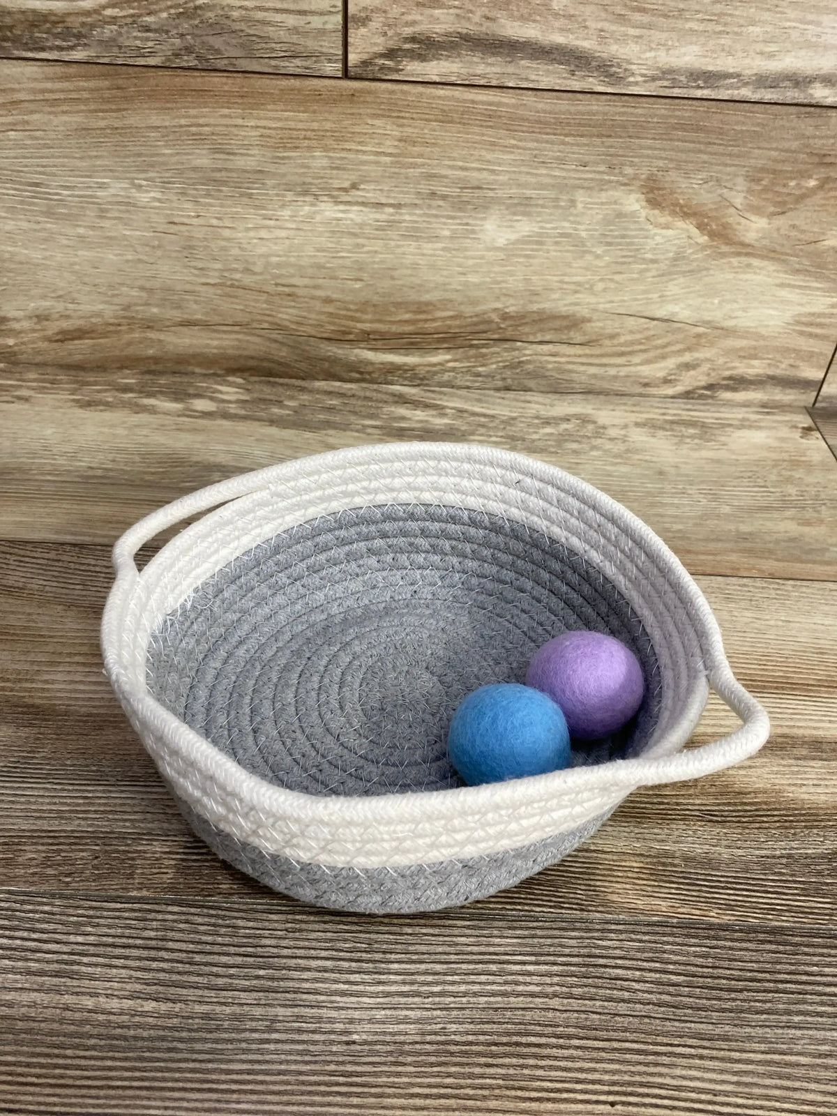 Gray woven storage basket with handles and two felt balls on wood surface