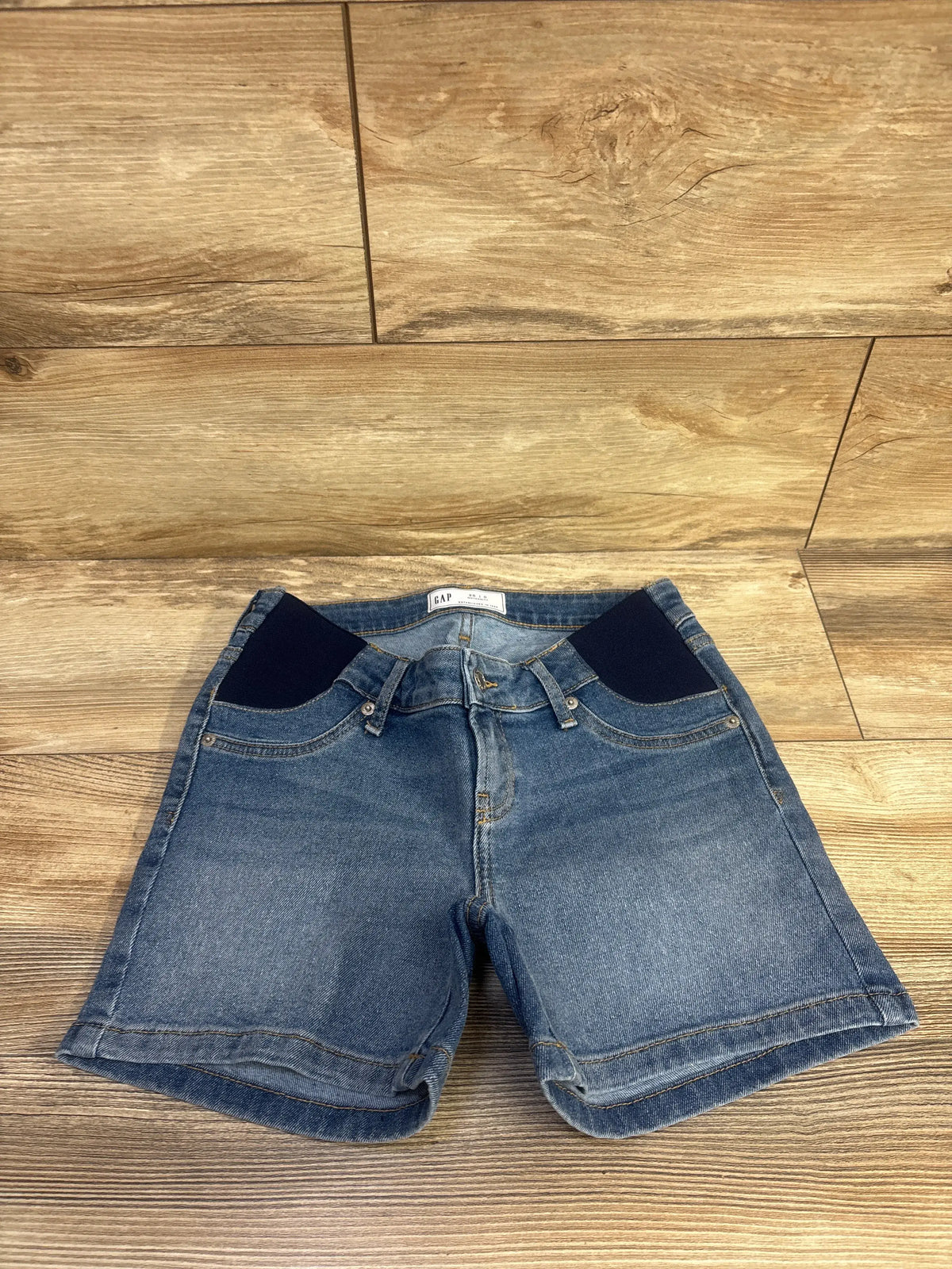 Front view of Gap maternity 4-inch inset panel denim shorts showcasing stretch denim and cuffed hems on a wood floor