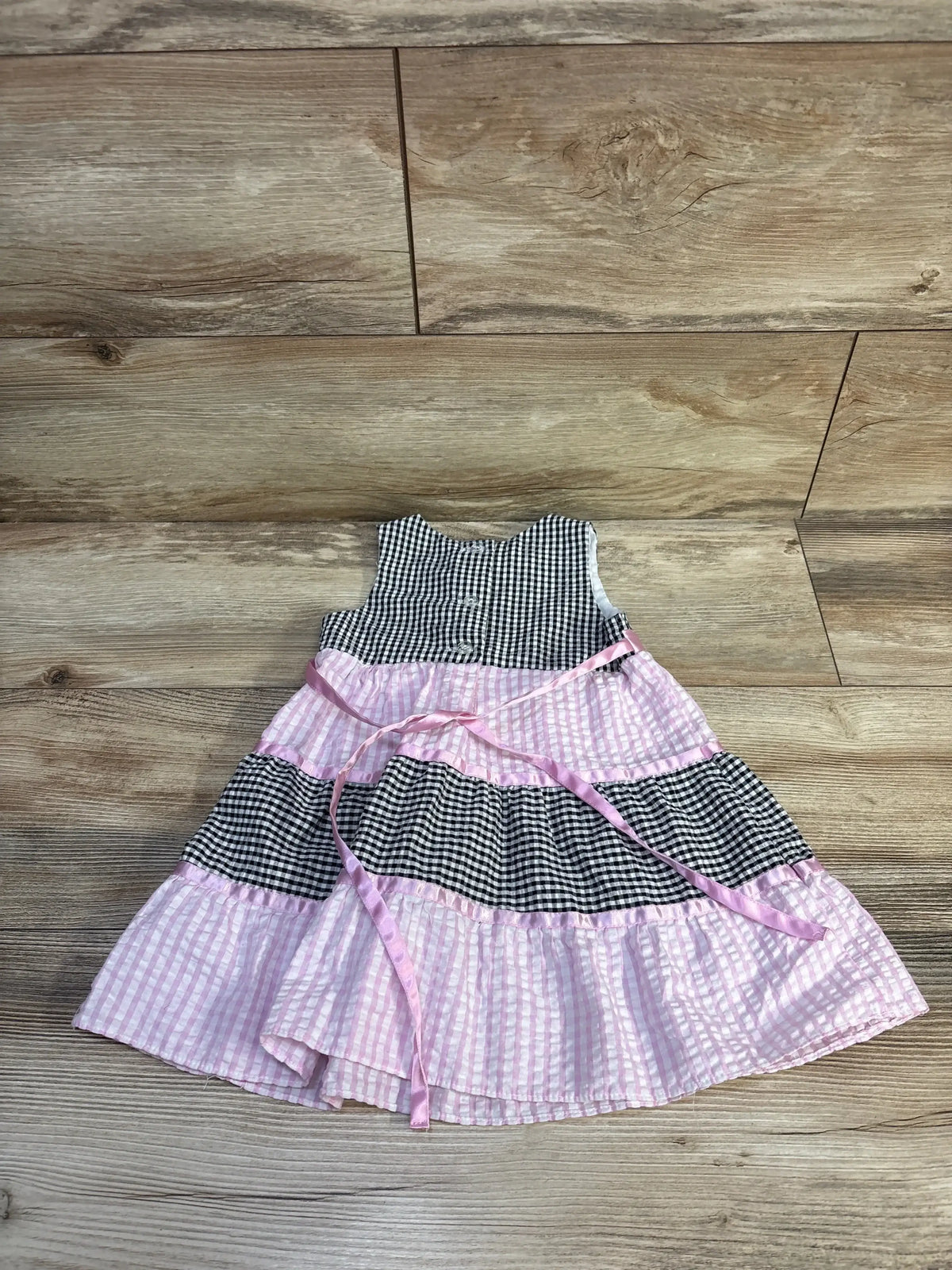 Flat lay of Rare Too! seersucker gingham dress with black-and-white and pink tiered panels and pink sash on wood floor