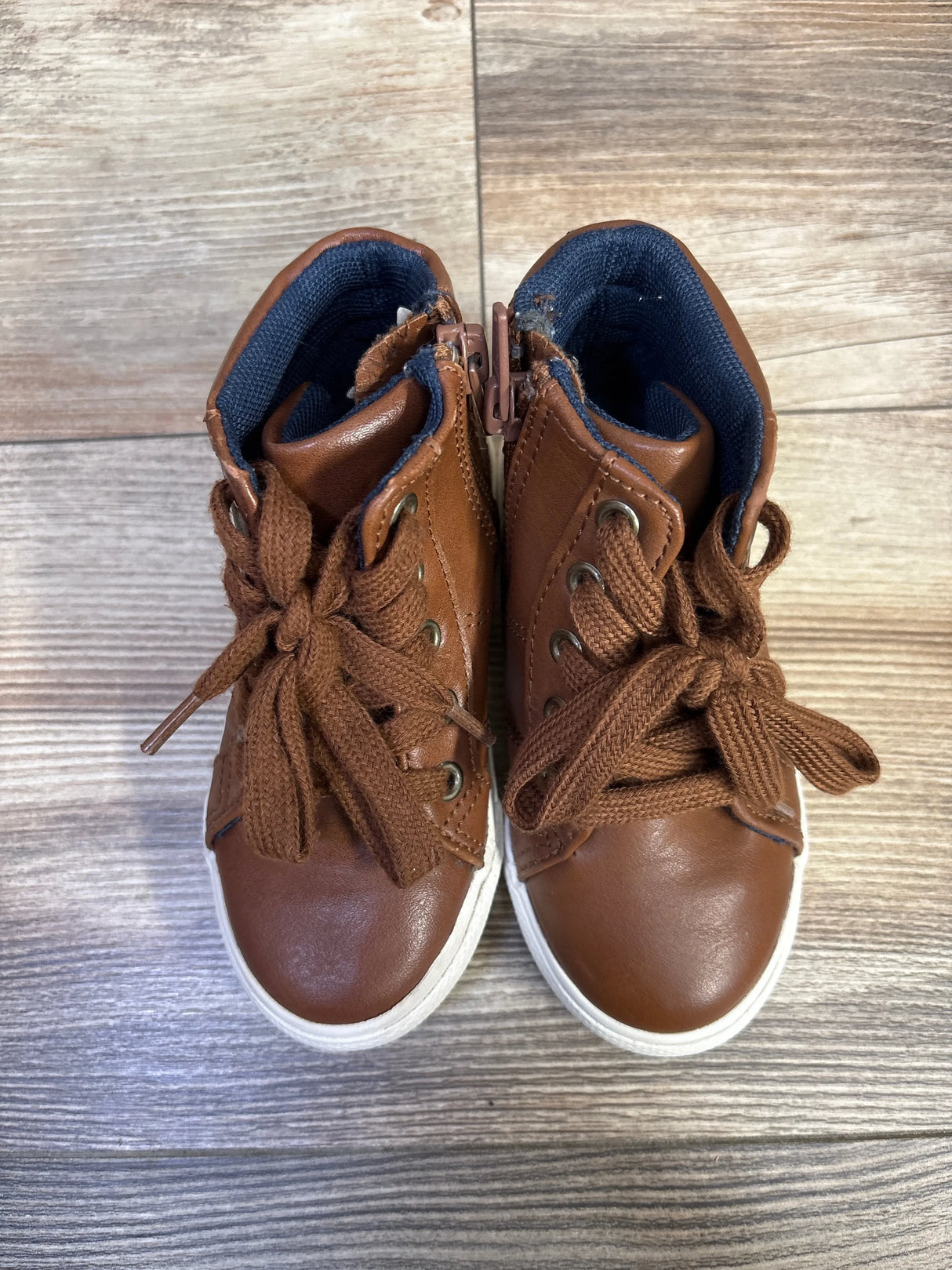 Top view of Cat and Jack brown high-top toddler sneakers showing tied laces, white soles, and navy lining on wood floor