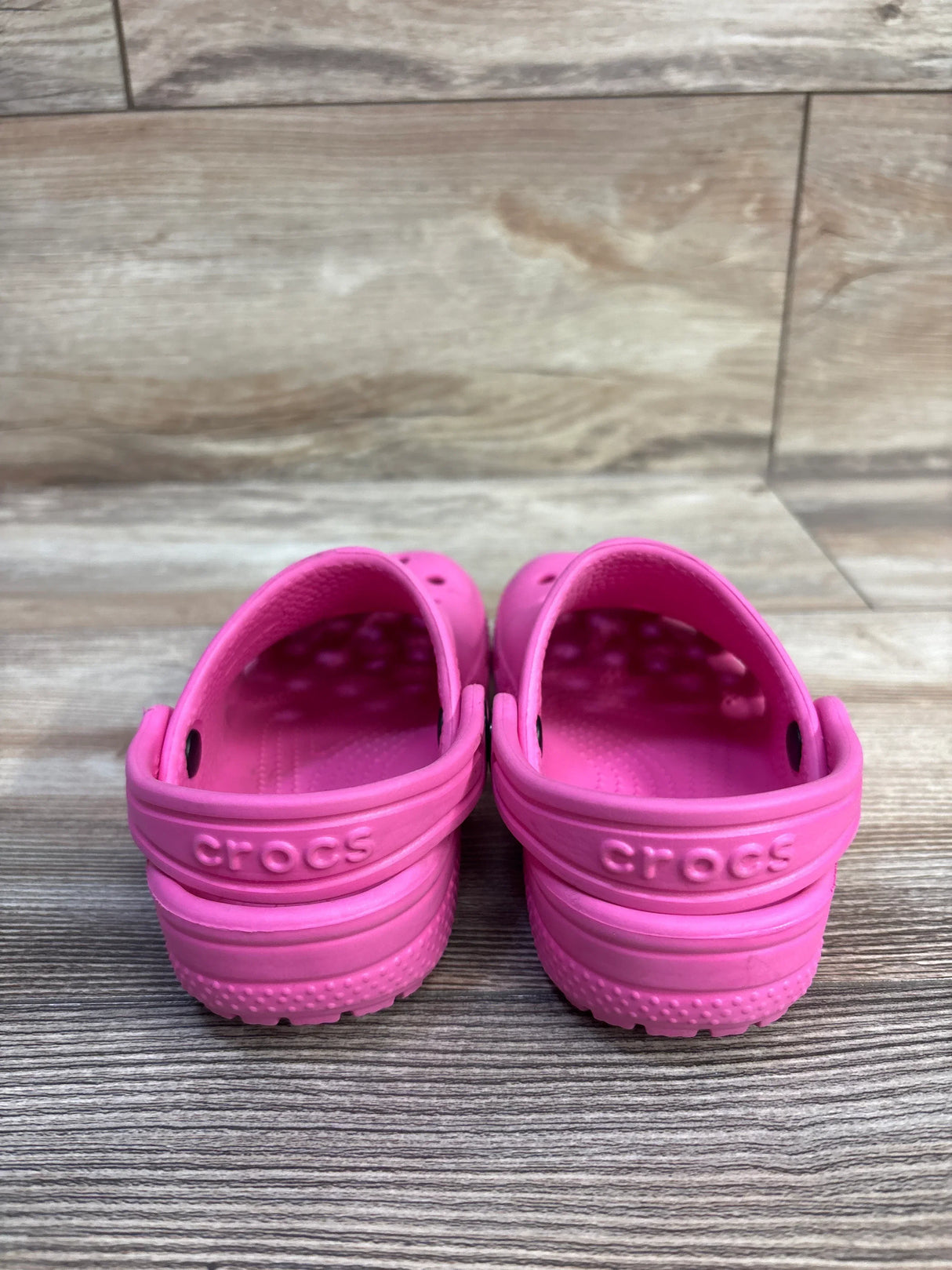 Rear view of pink Crocs Classic Clog, size 9C, showcasing heel strap and embossed Crocs logo on wood floor background