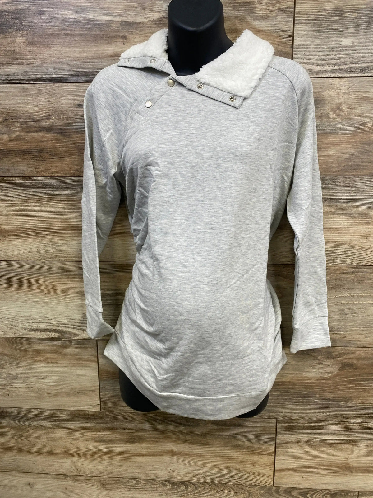 Front view of grey maternity sweatshirt with sherpa snap collar and side ruching on black mannequin against wood background