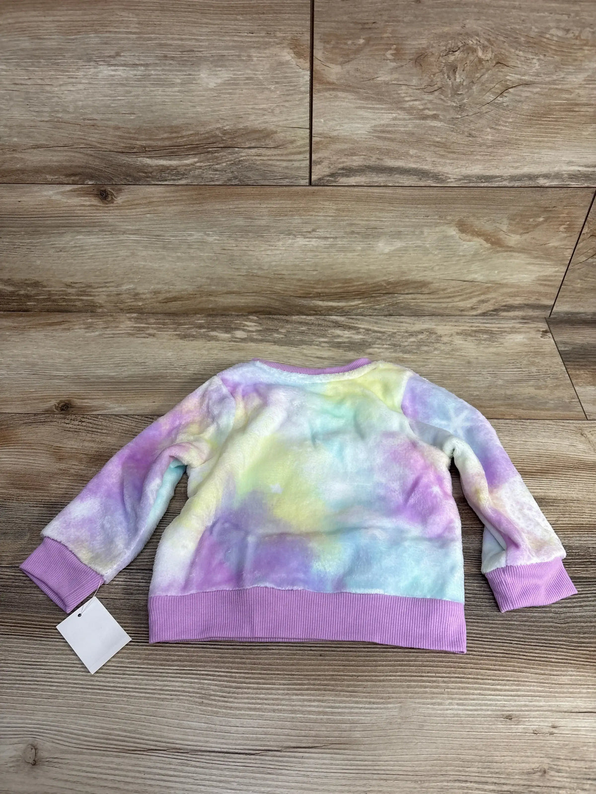 Pastel tie-dye toddler sweatshirt with purple ribbed cuffs and hem on wood floor