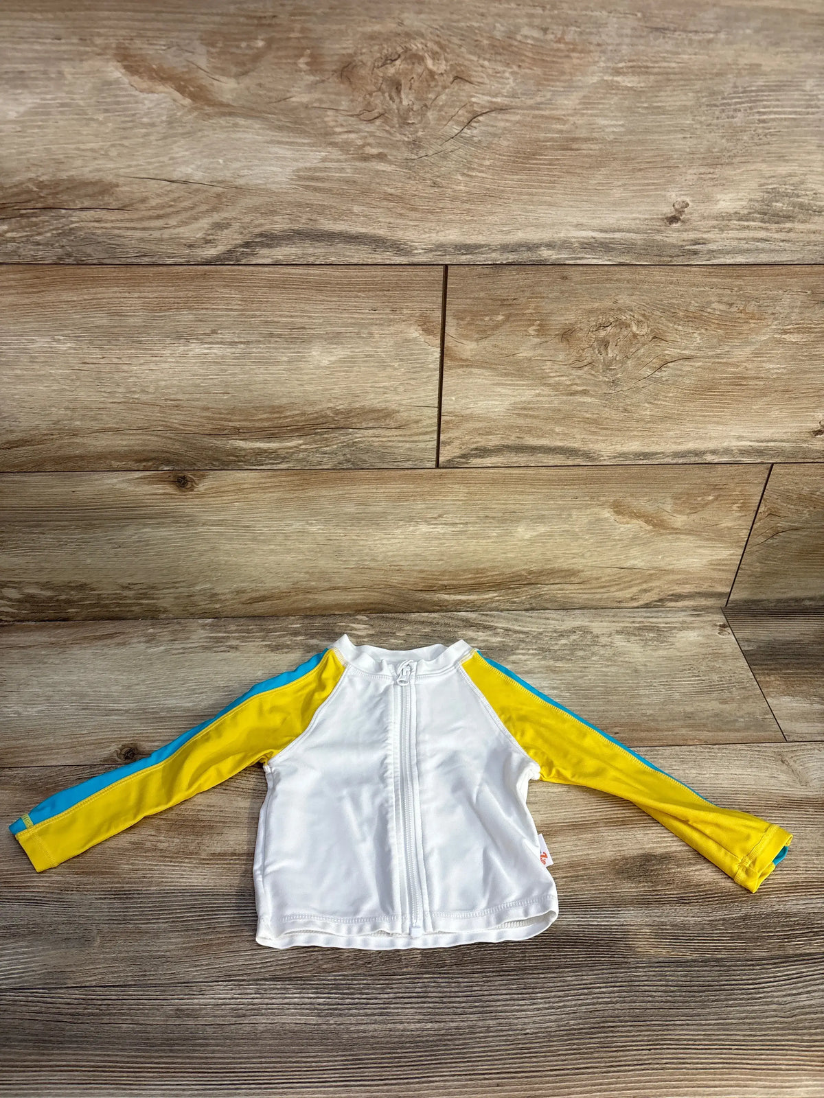 Front view of white long-sleeve zip-up rash guard shirt, size 12 months, with yellow sleeves and blue trim on wood floor