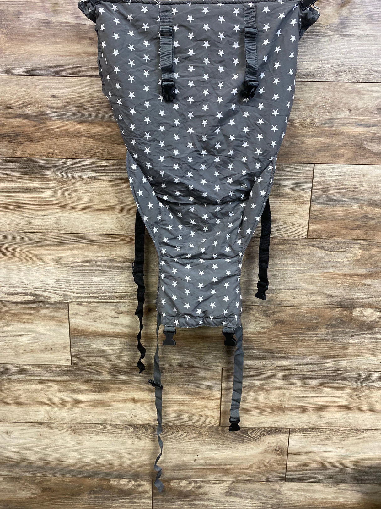 Front view of baby high chair harness showing grey fabric with white stars and adjustable black straps on wood floor