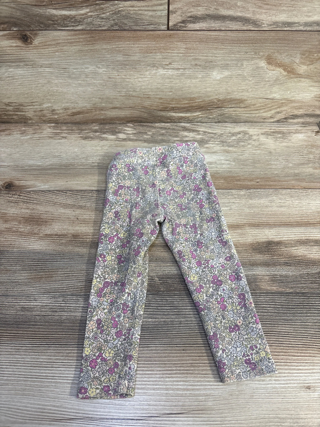 Front view of cream ribbed girls leggings size 18 months showing all over purple and yellow floral print on wood floor background