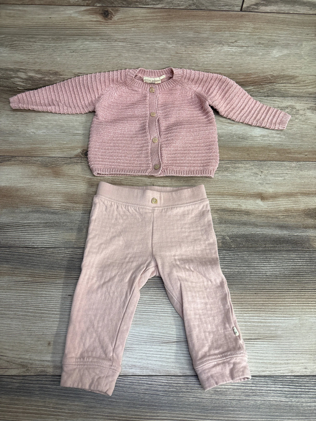 Pink knit baby cardigan and matching pants outfit set on wooden background