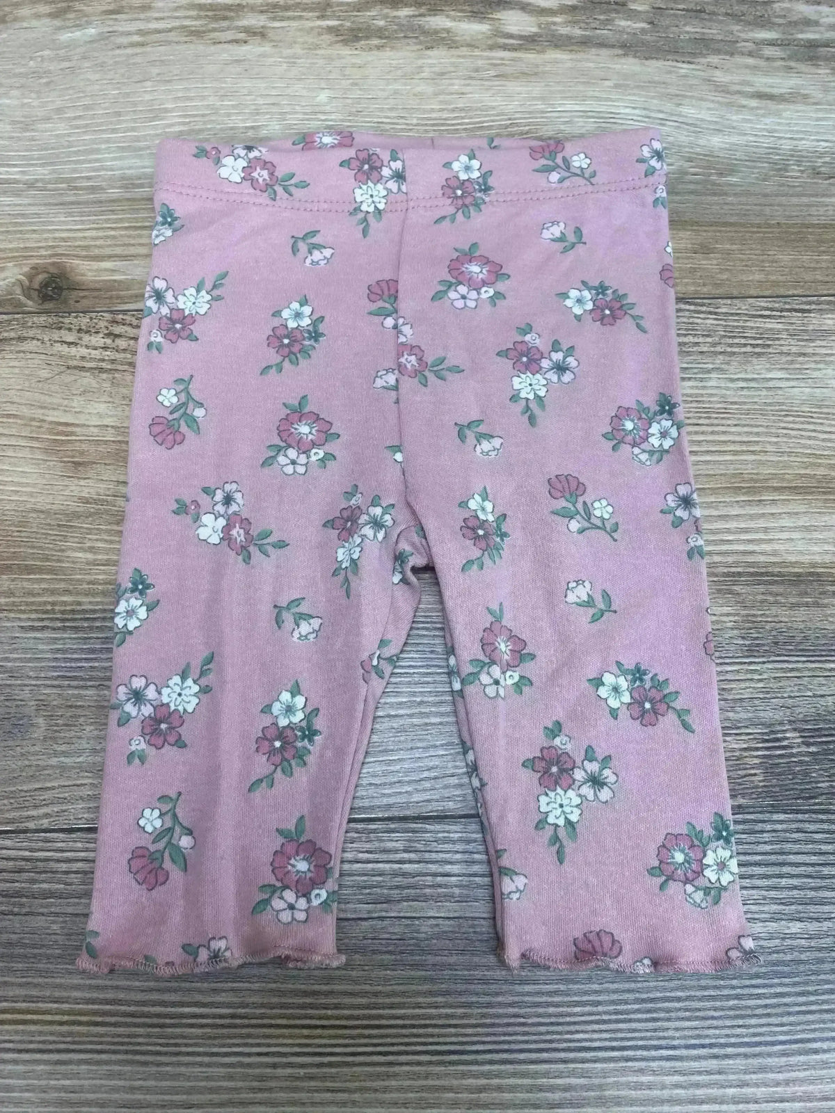 Top down view of pink Tahari floral baby leggings size 0 to 3 months showing all-over white and mauve flower print on wood background