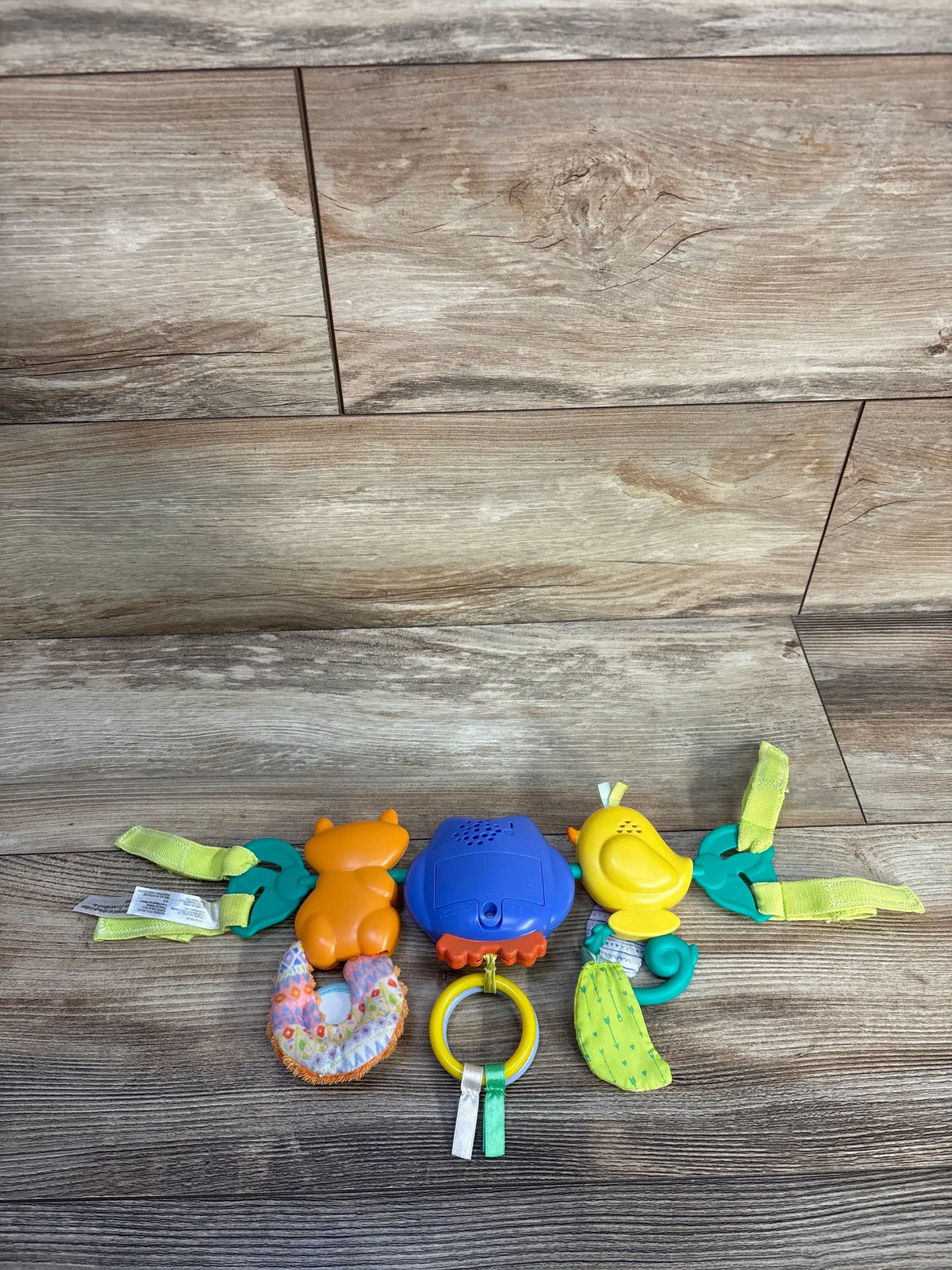 Front view of Infantino Go gaga! Musical Travel Bar Activity Toy showcasing colorful sensory toys, ribbons, ring, and fasteners on wood floor