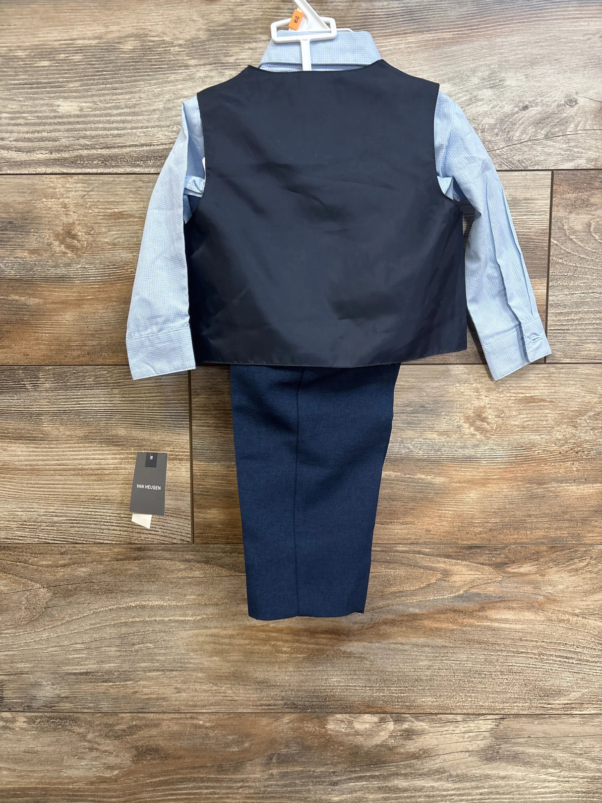 Back view of 4-piece Van Heusen toddler suit showing navy vest back, light blue shirt sleeves, and navy pants on wood floor