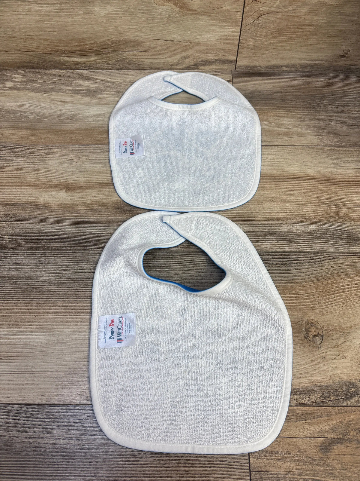 Back view of WinCraft 2pk Detroit Lions All-Pro Drool Bibs showing white polyester backs and blue trim on a wood surface