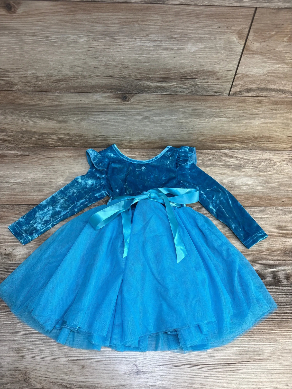 Blue velvet long sleeve toddler dress with tulle skirt and ribbon bow, laid on wood floor