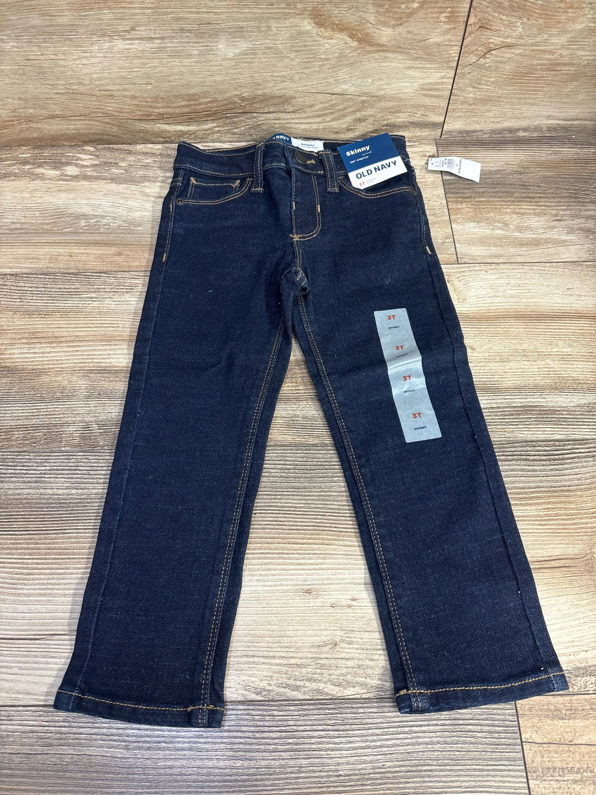 Flat lay of Old Navy 360 Stretch skinny jeans, toddler 3T, dark indigo wash showing front pockets and brand tag on wood floor