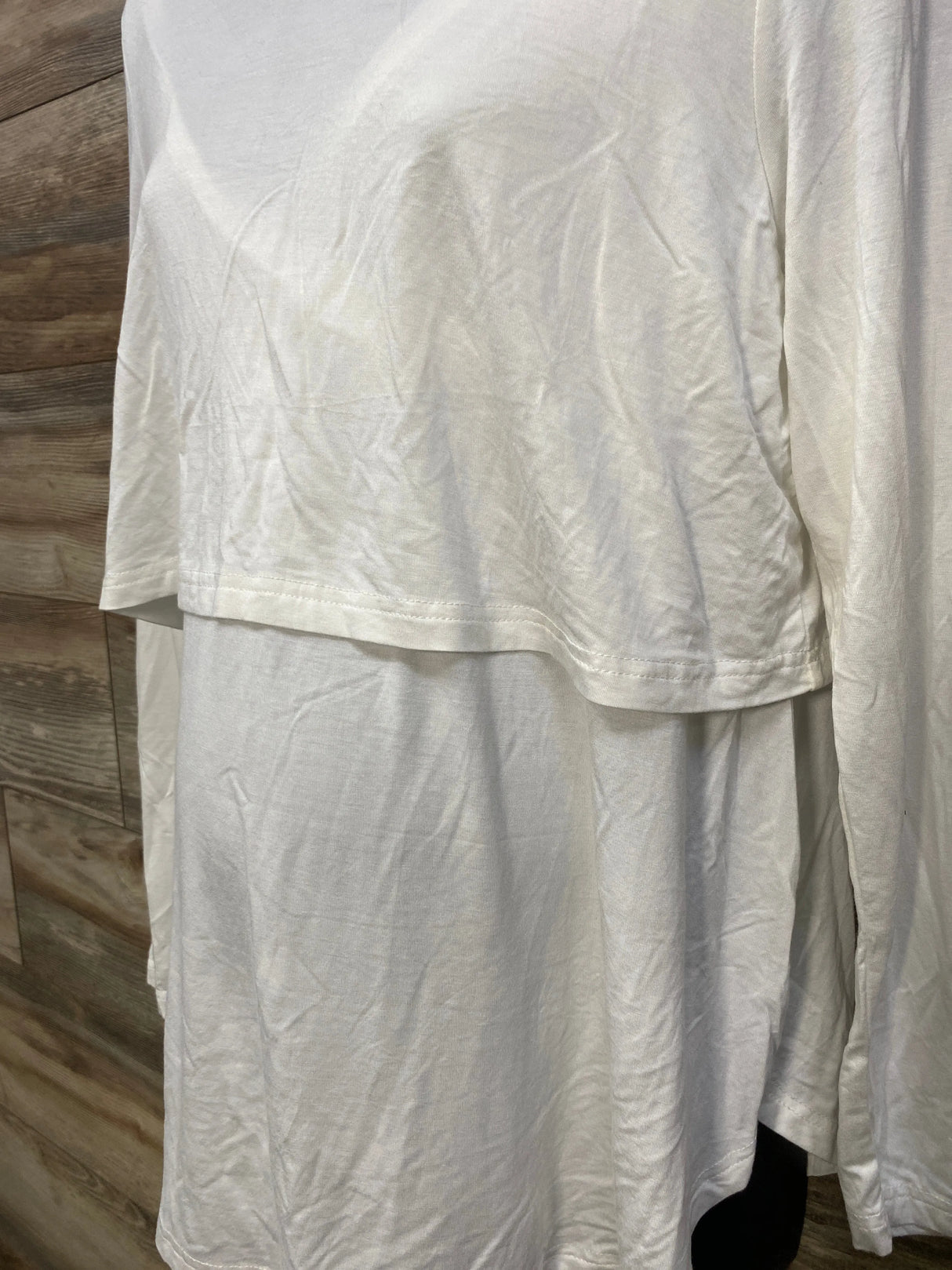 White long-sleeve layered cotton shirt hanging on wooden background