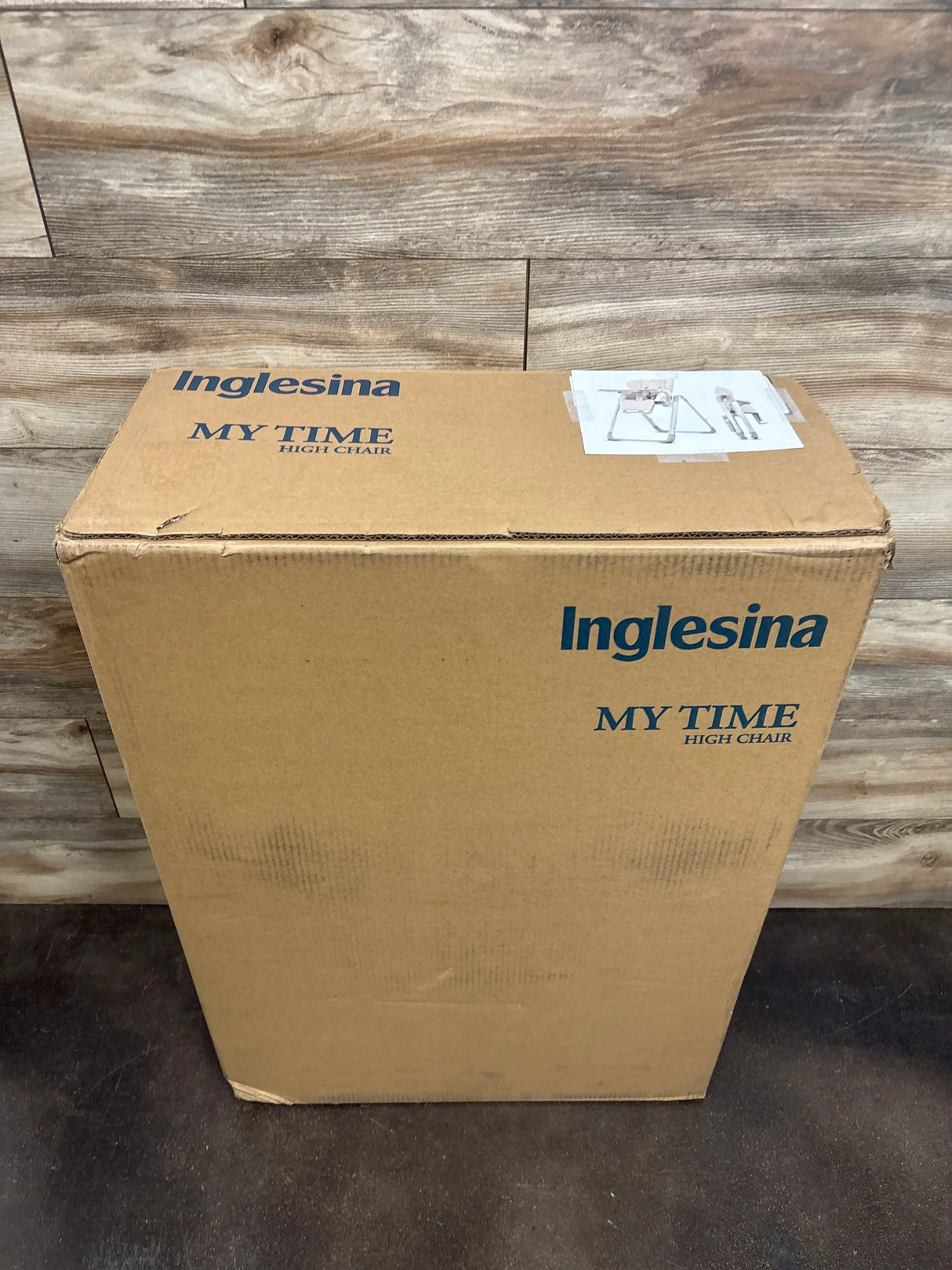 Cardboard box with Inglesina My Time high chair packaging against wood panel wall