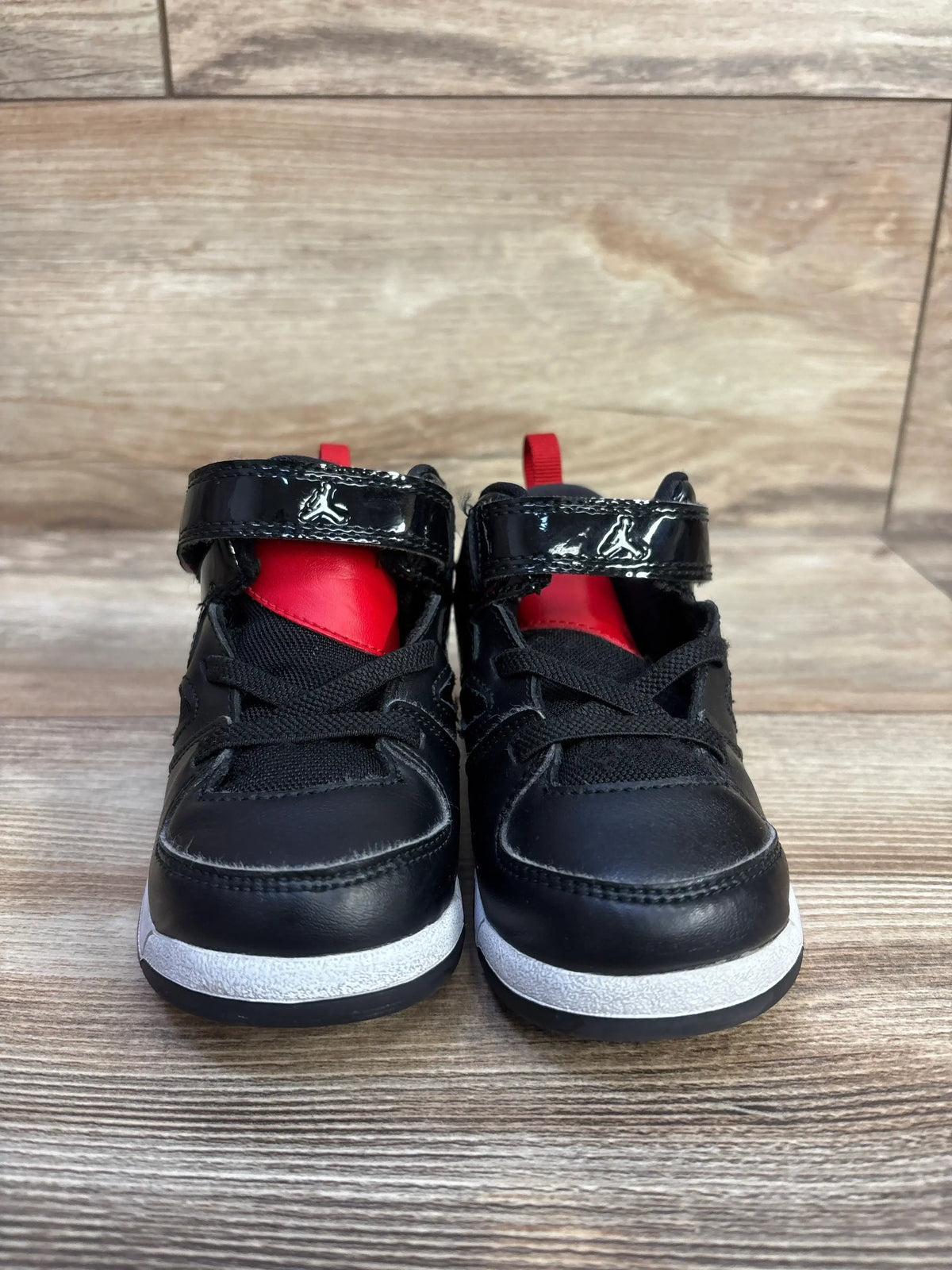 Front view of toddler Air Jordan Bred sneakers showing black leather, red tongue, patent velcro strap on wood floor