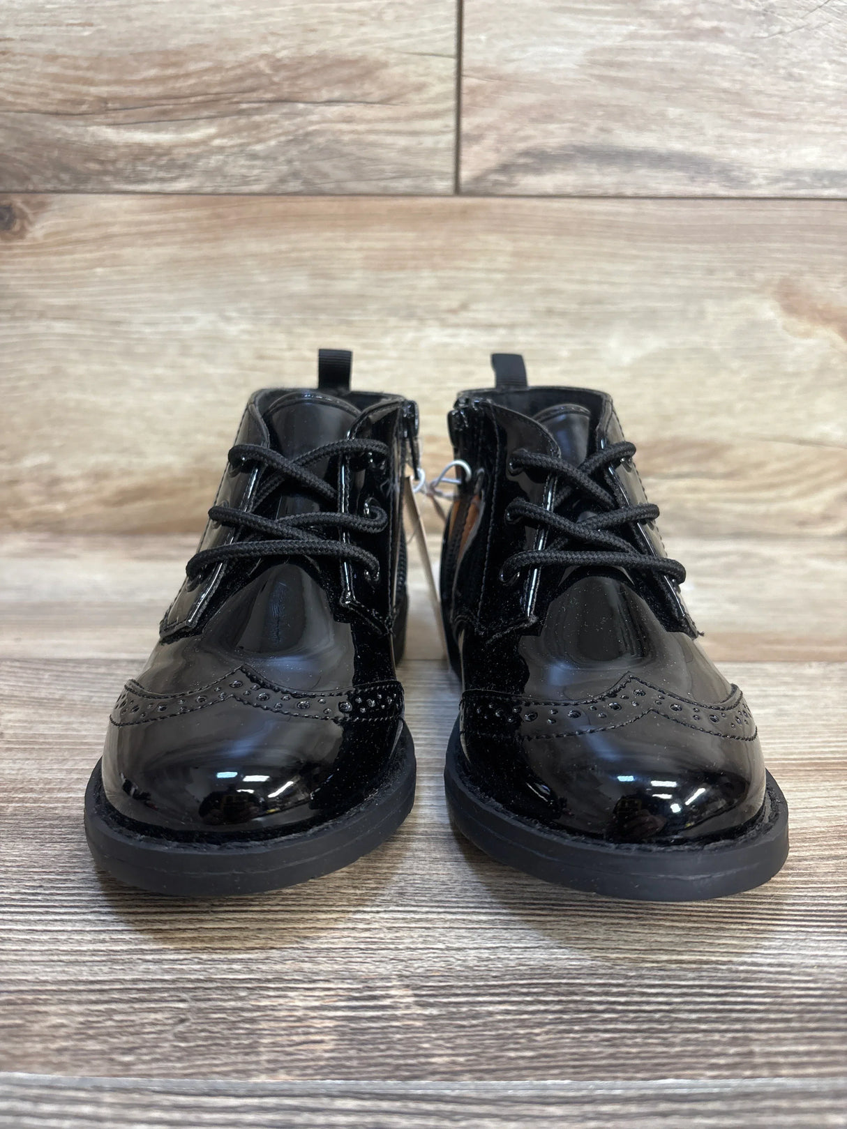 Black patent leather toddler dress shoes with laces and side zippers on wood floor