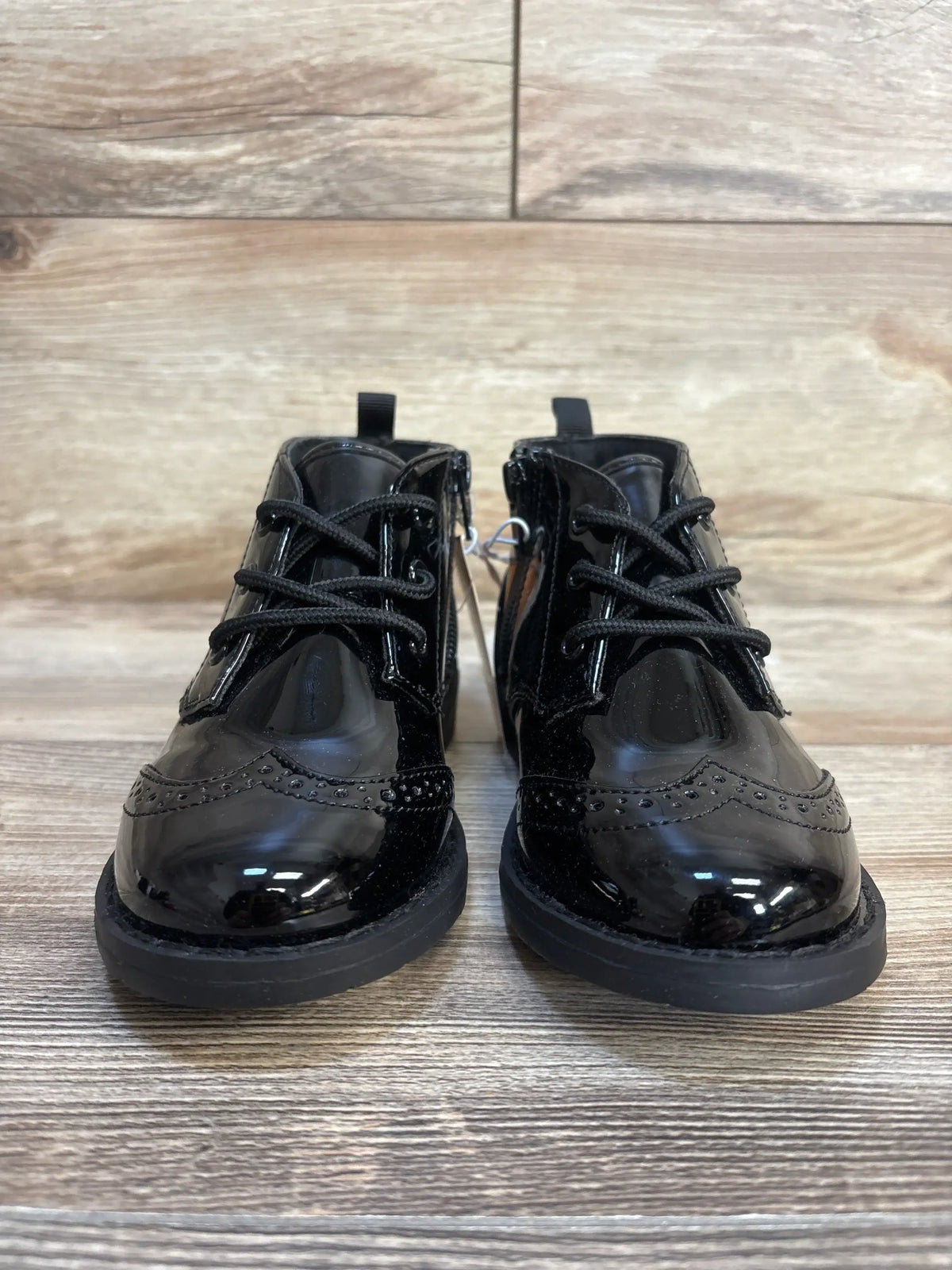 Black patent leather toddler dress shoes with laces and side zippers on wood floor