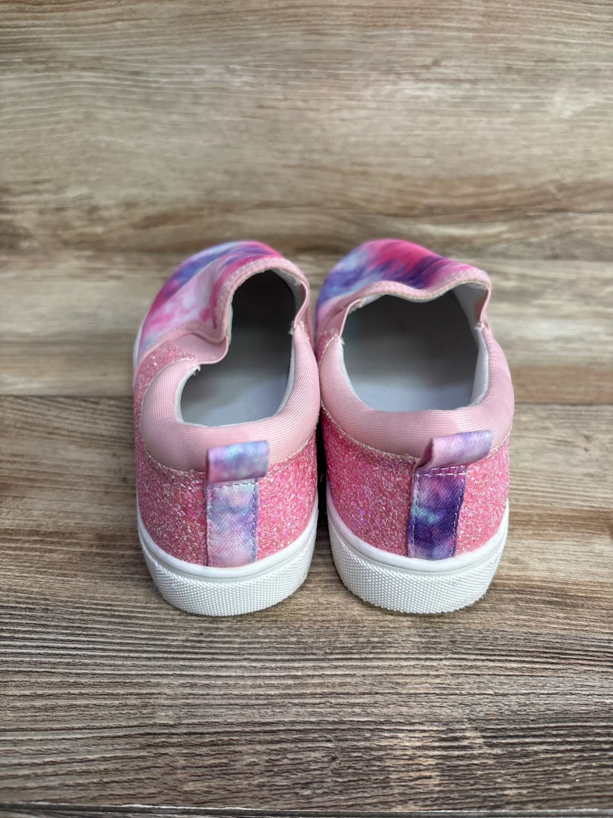Pink and purple toddler slip-on shoes with glitter fabric and white soles on wooden floor