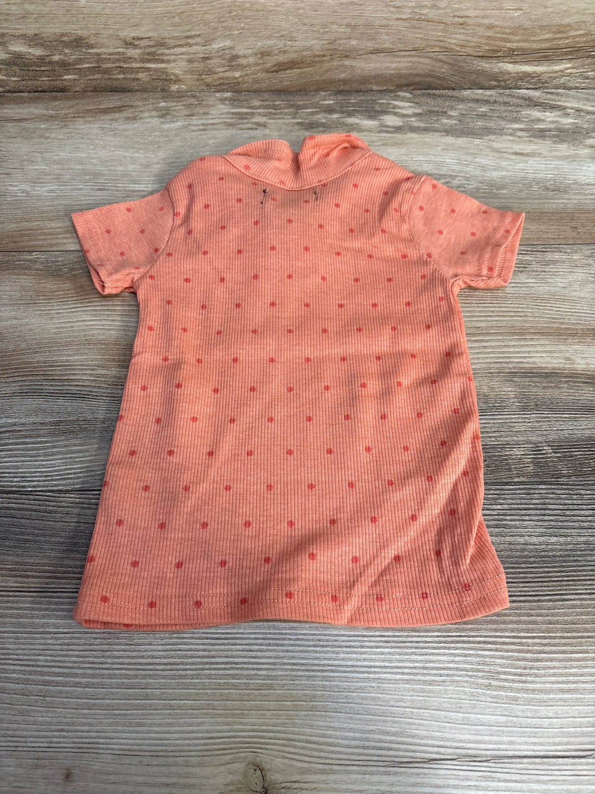 Back view of peach toddler polo shirt with small red polka dots and ribbed texture, size 24 months, on light wood background